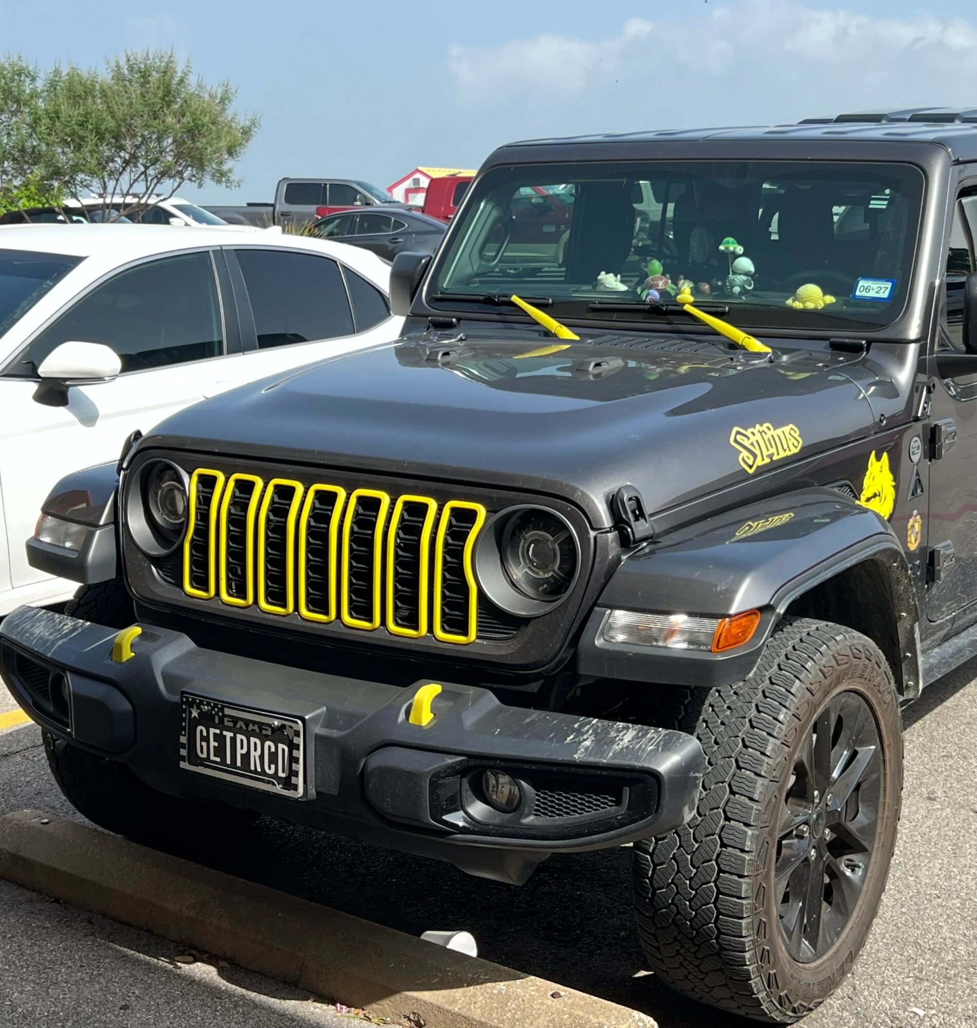 Black Jeep with yellow accents parked outdoors, with other vehicles and trees in background.