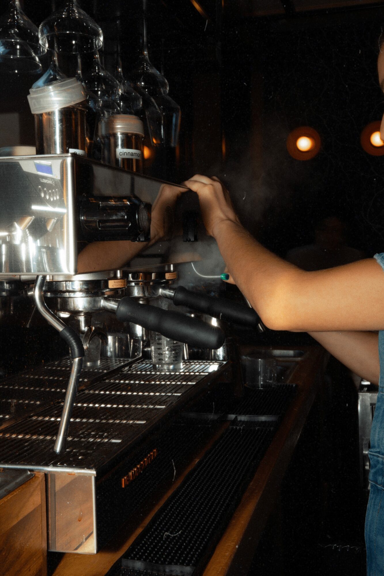 Person operating a professional espresso machine in a dimly lit environment.