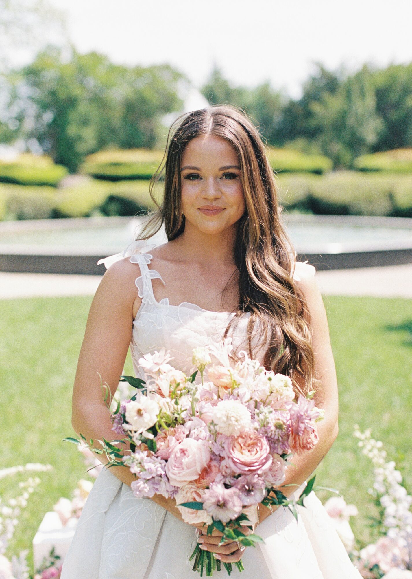 Young woman in a white dress holding a large bouquet of pink and white flowers outdoors.
