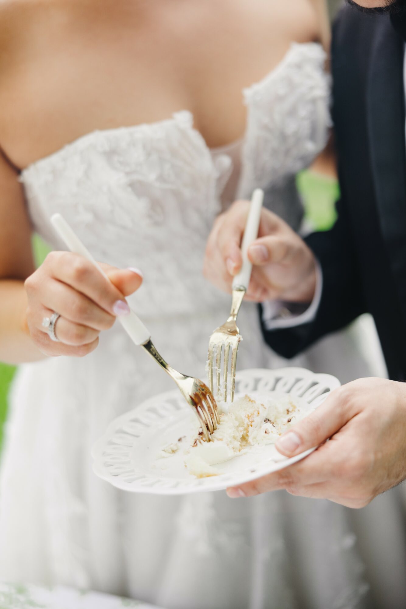 Bride and groom cut wedding cake together, holding knives and plate with cake slices.