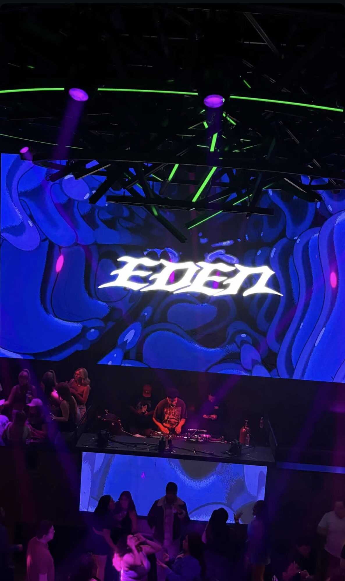 Stage with a DJ, large screen displaying 'Eden', and audience in front, colorful lighting and visuals.