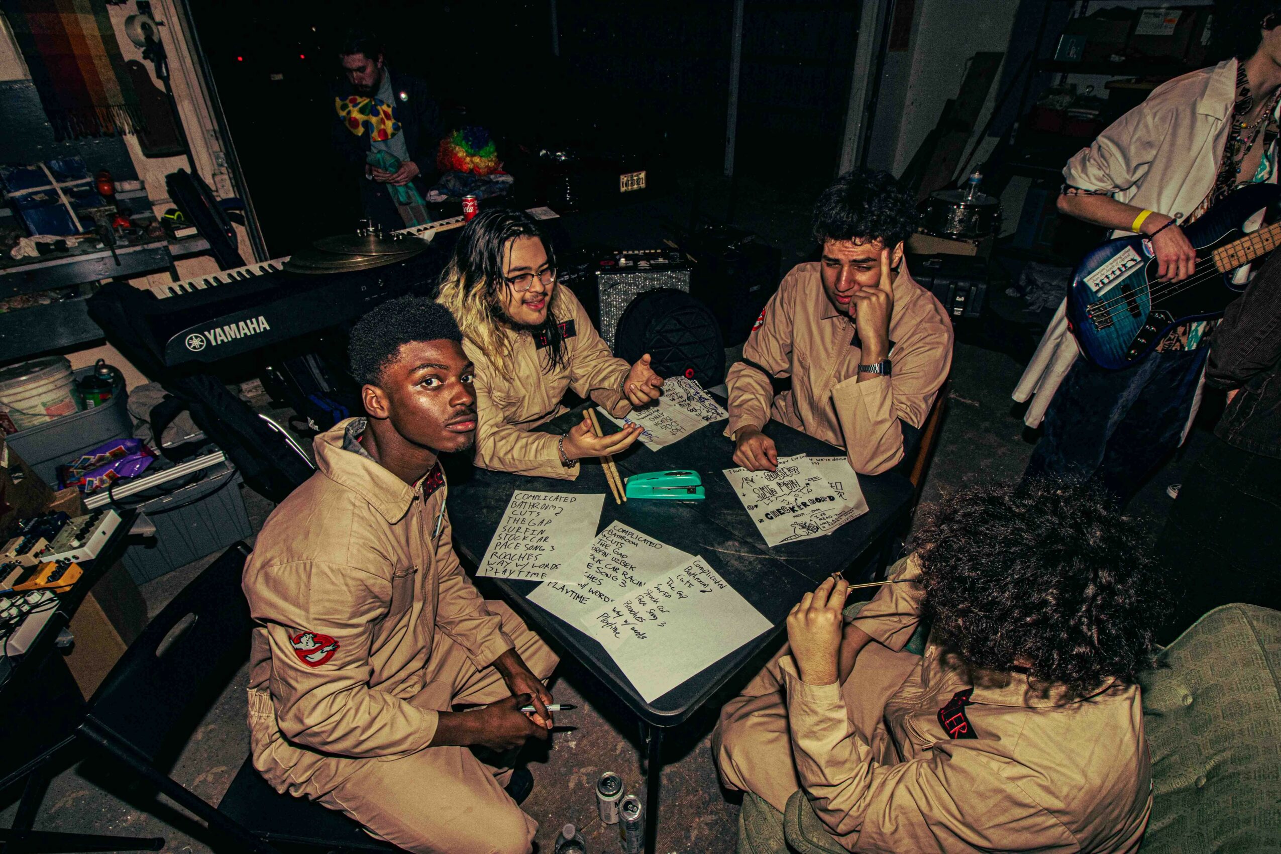 Group of five people sitting around a table with papers and a laptop, in a music studio or rehearsal space.