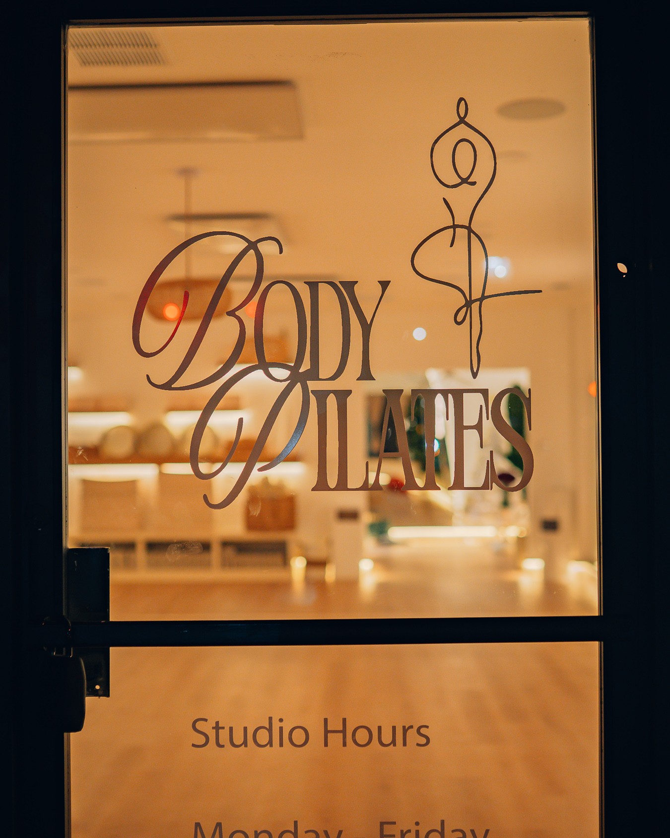 Glass window with the words 'BODY' and 'DAMES' and a stylized figure logo, reflecting interior lighting.