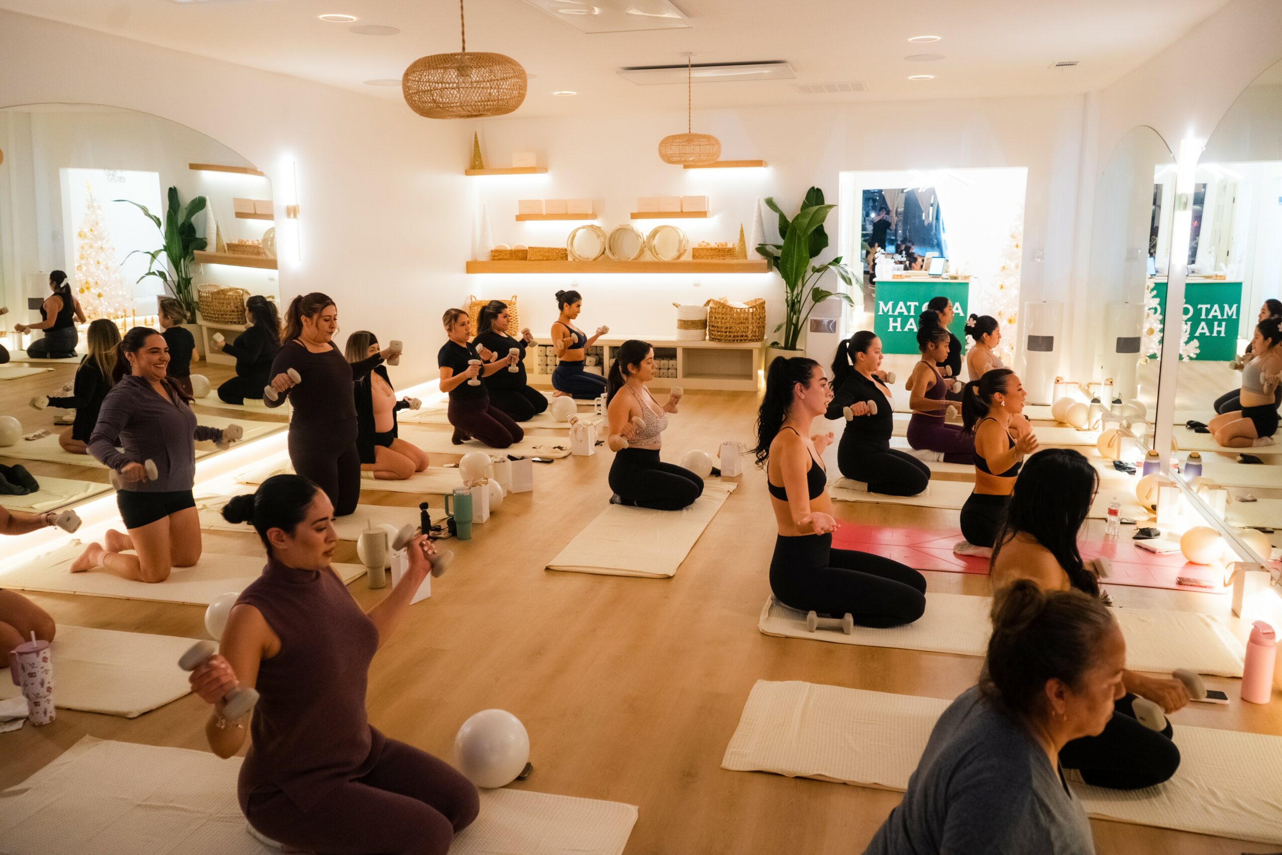 Group of people practicing yoga in a bright, spacious studio with mats, shelves, and plants.