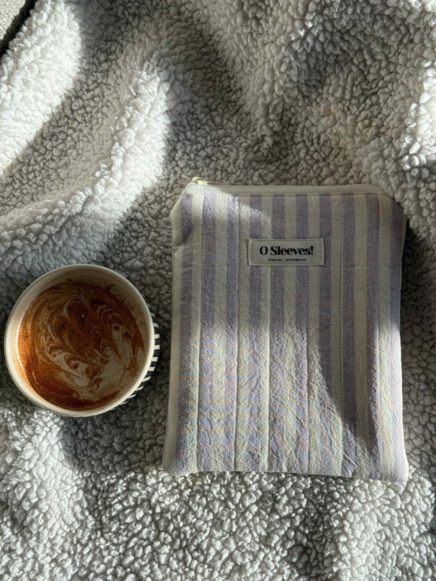 Striped tissue box and a cup with a brown liquid on a textured blanket.