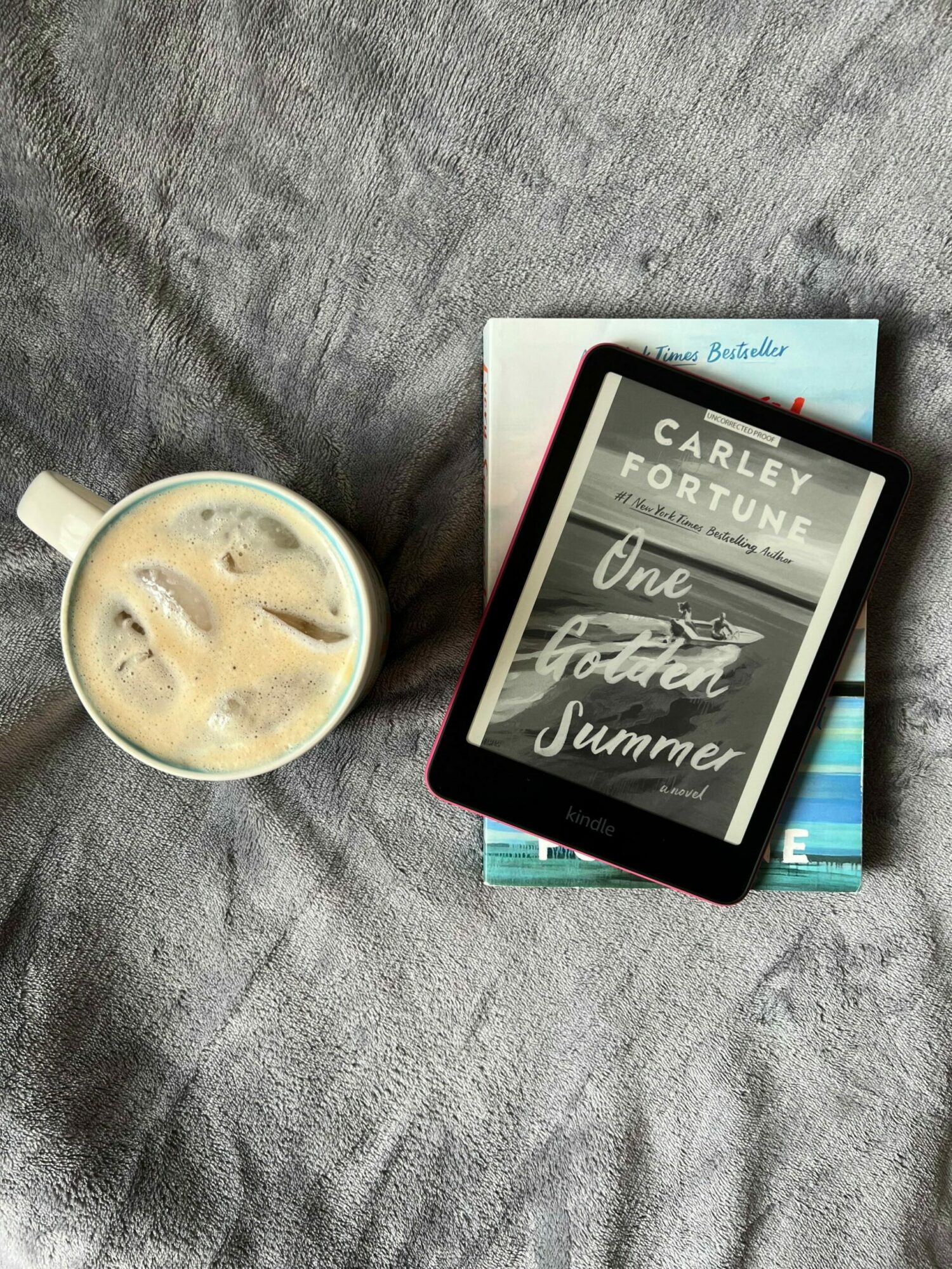 Tablet, books, and a cup of iced coffee on a gray fabric surface.