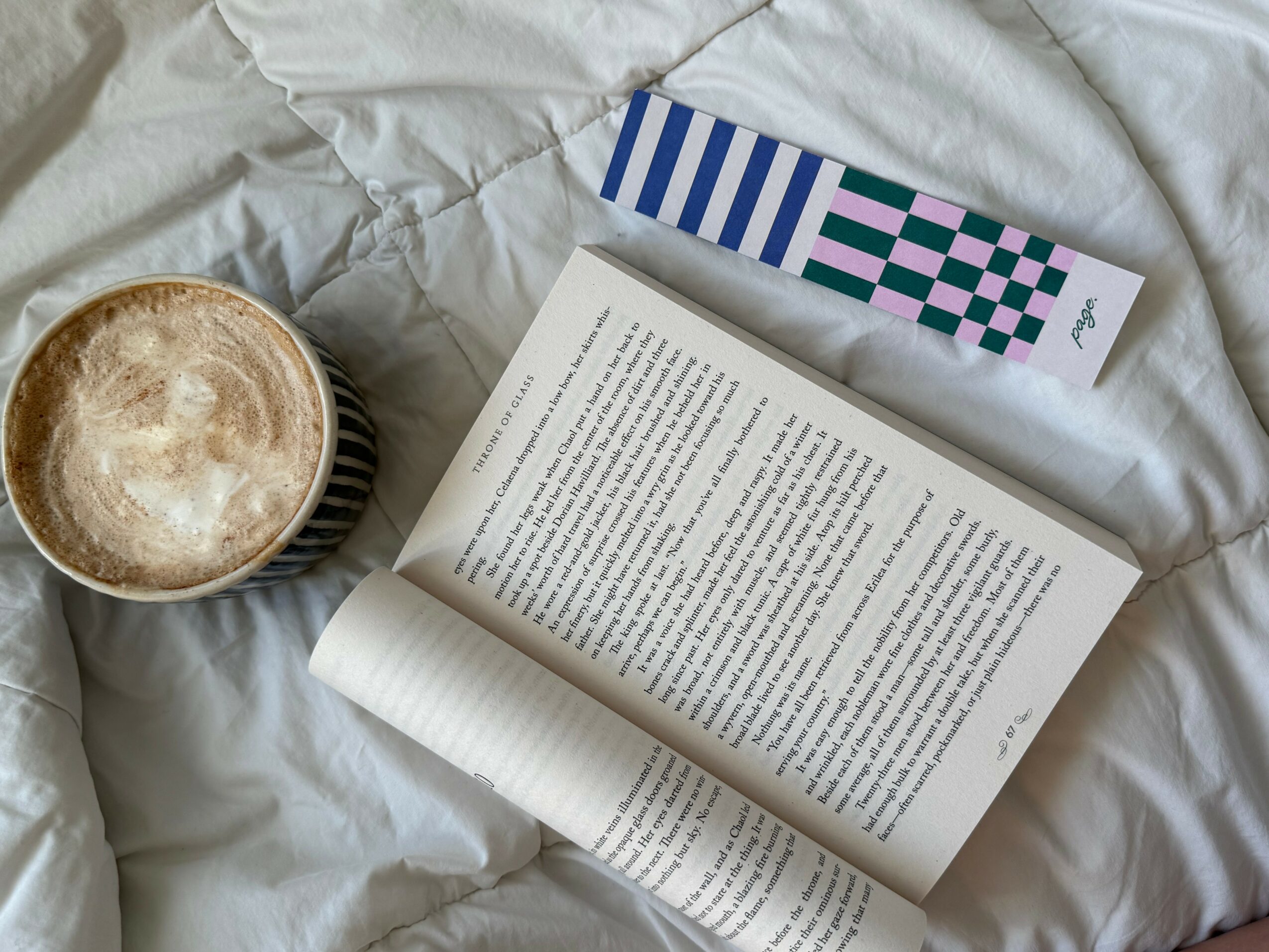 Open book on a bed with a cup of coffee and a patterned box nearby.