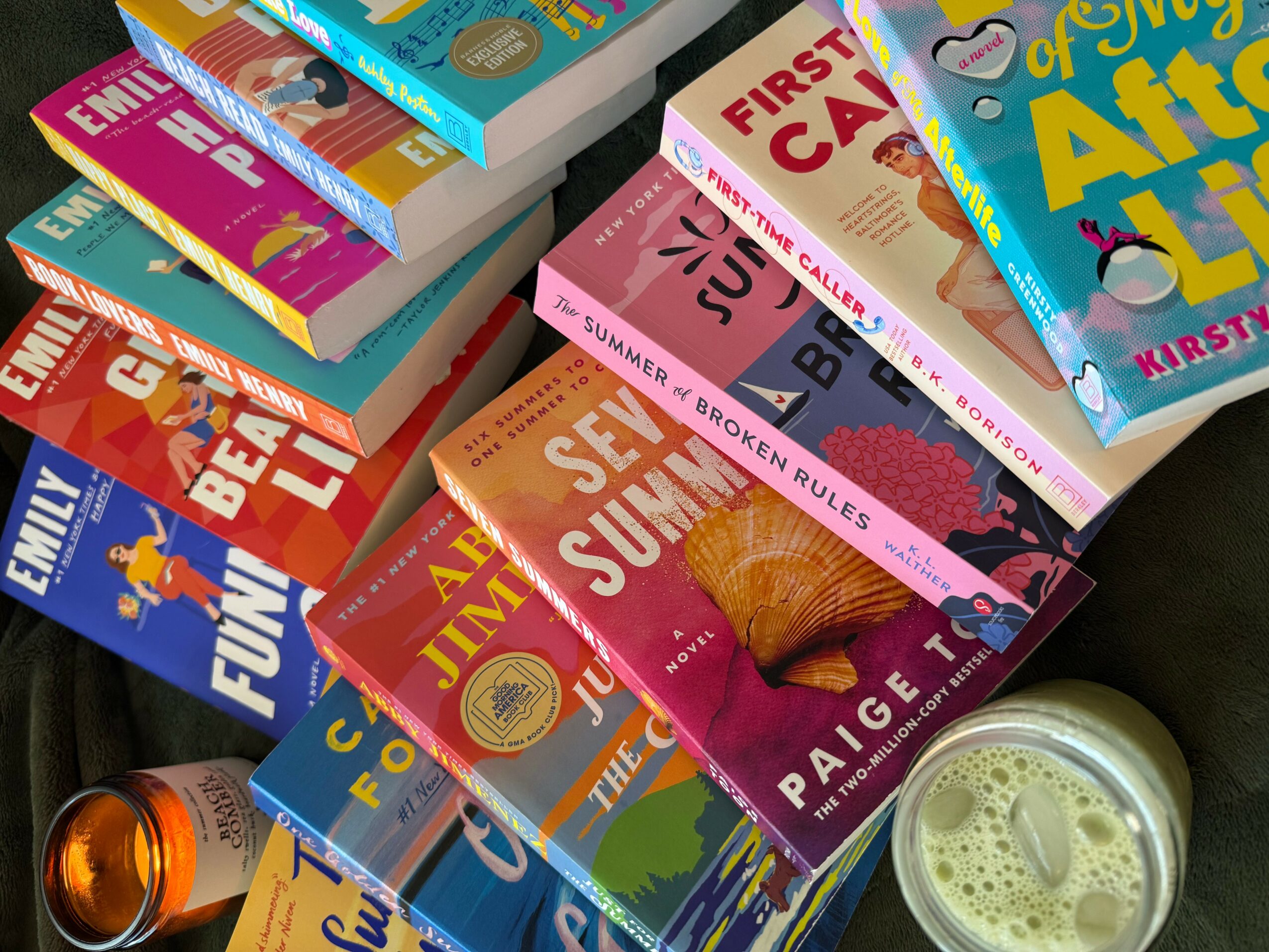 Stack of colorful children's books and a glass of beverage on a table.
