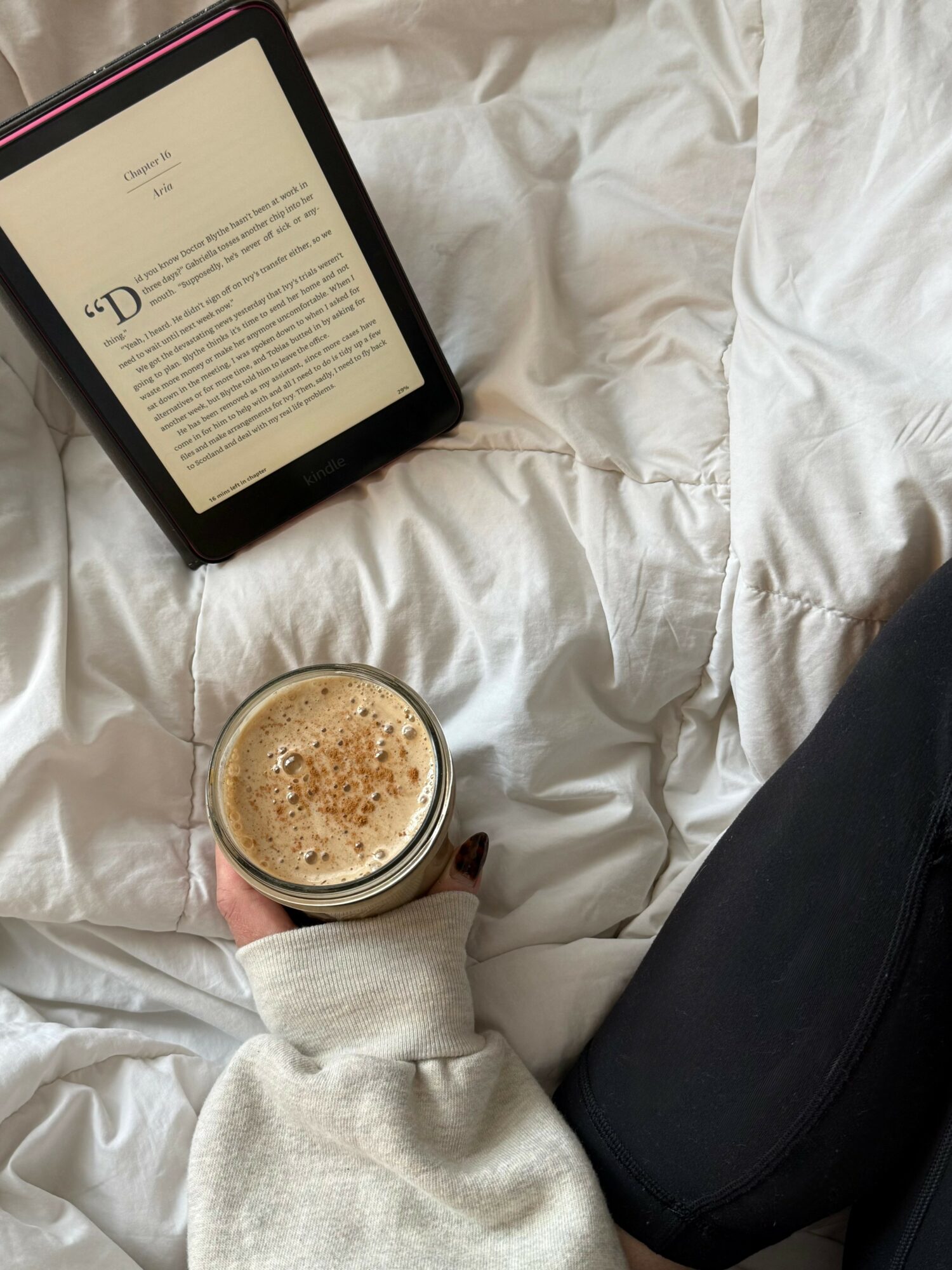 Person holding a cup of coffee with a tablet on a bed with white sheets.