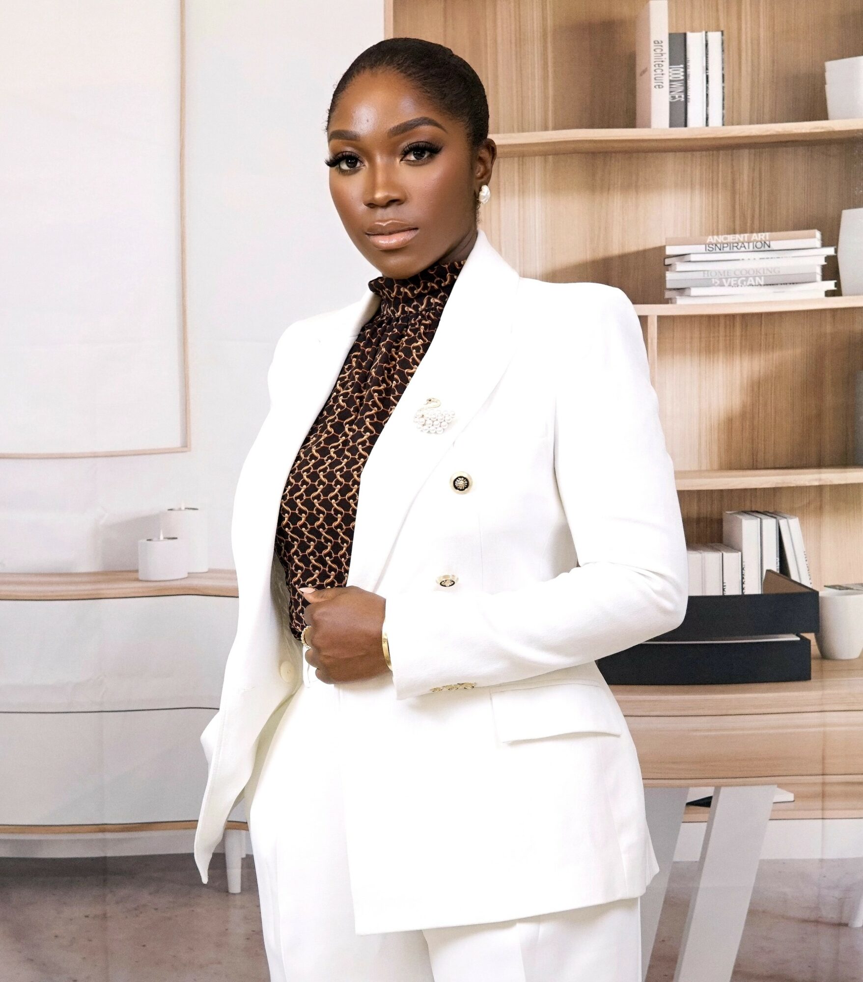 Woman in white blazer and leopard print top standing in modern office with wooden shelves.