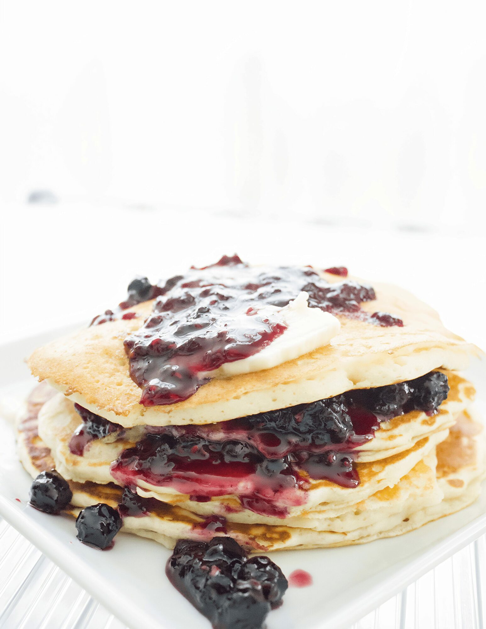 Stack of three pancakes with berry syrup and fresh berries on a white plate.