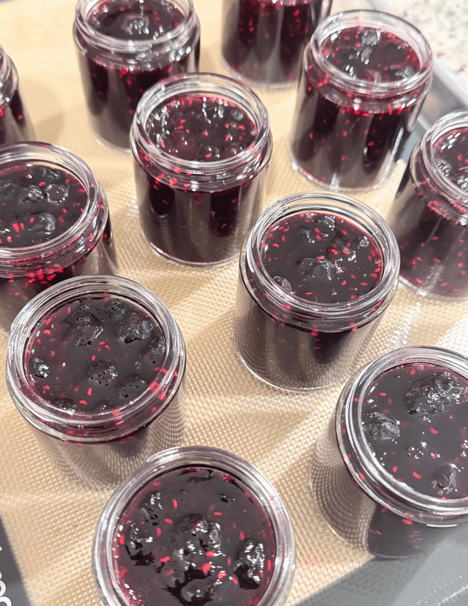 Multiple small jars filled with dark purple liquid, some with bubbles on the surface, arranged on a beige surface.