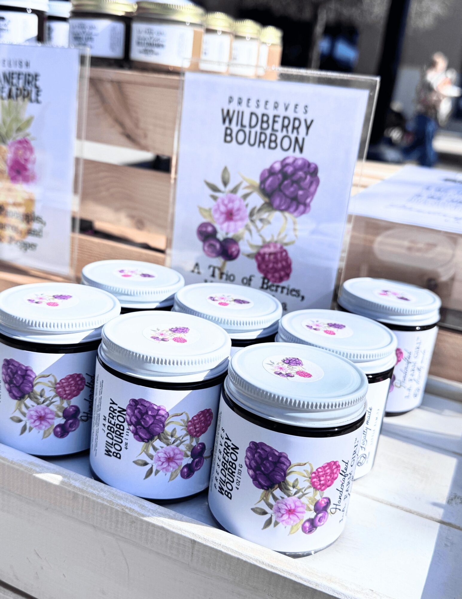 Small jars with purple berry illustrations on a display table at an outdoor market.