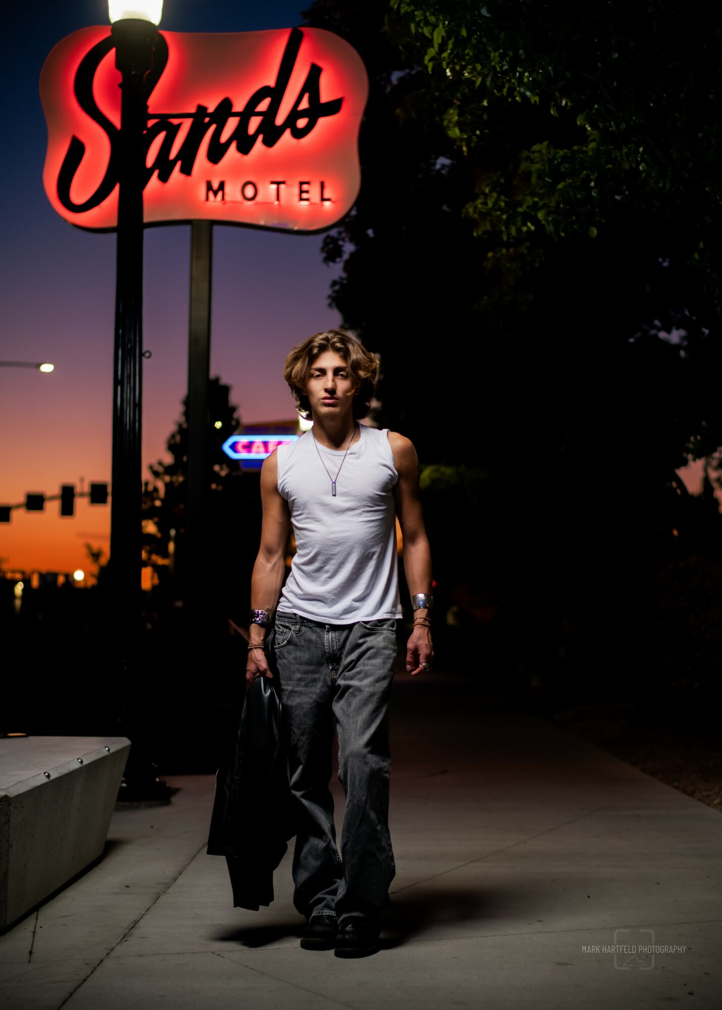 Person walking on sidewalk at night near a motel sign with trees in background.