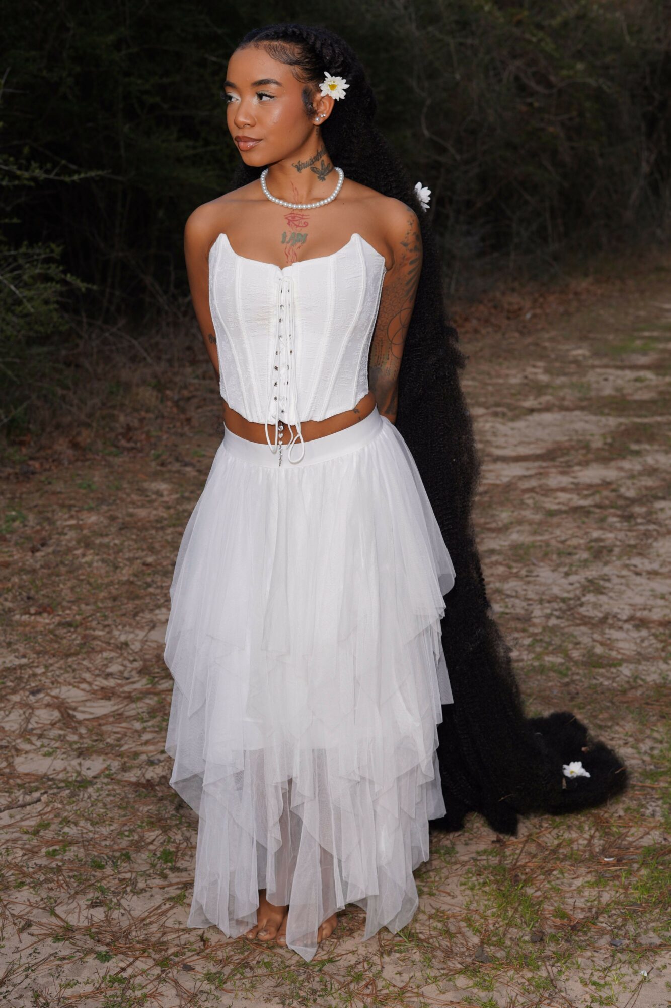 Woman in white dress with layered skirt and corset top, standing outdoors with trees in background.