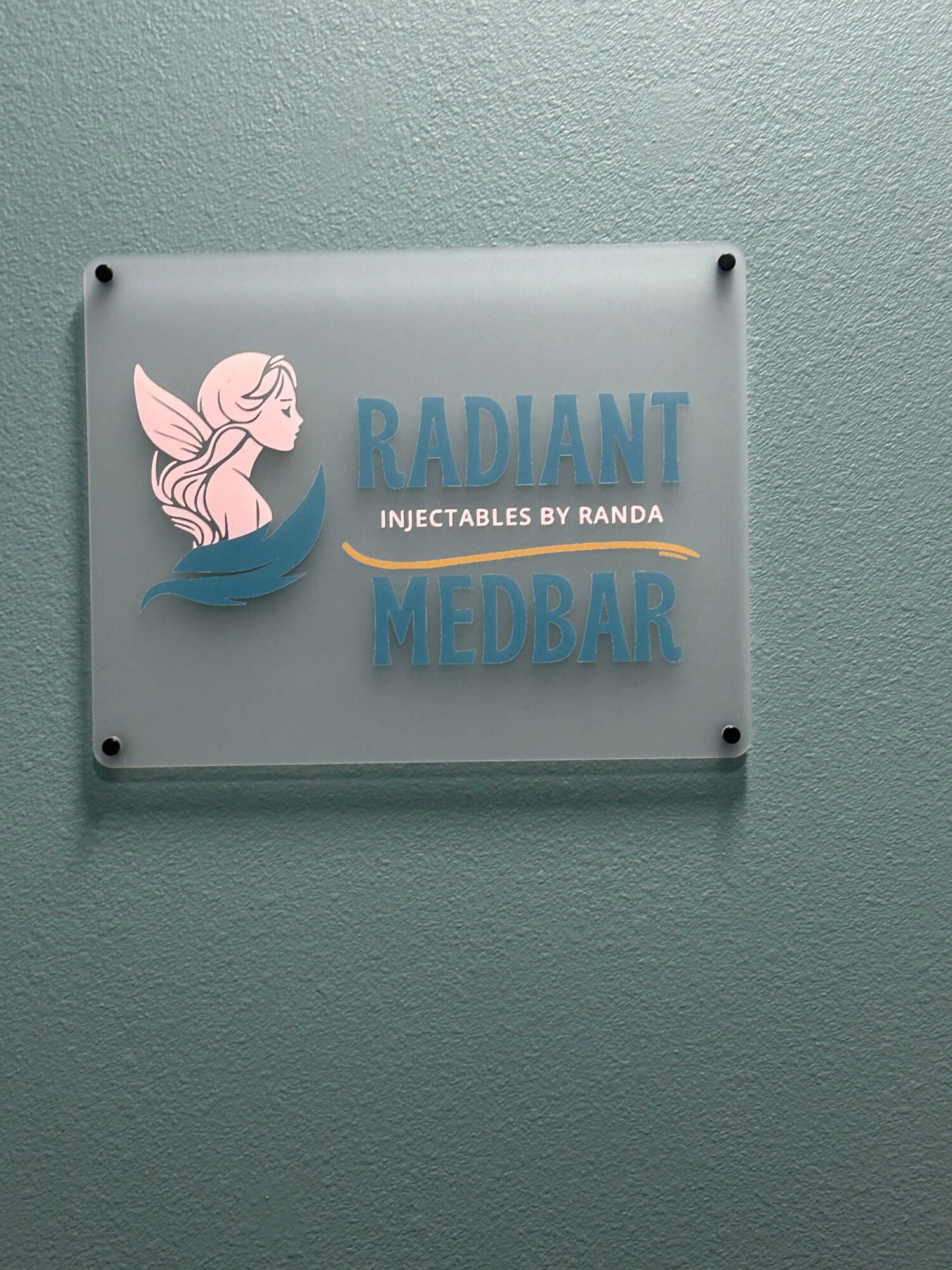 Sign with a fairy illustration, text 'RADIANT MEDBAR', mounted on a wall.