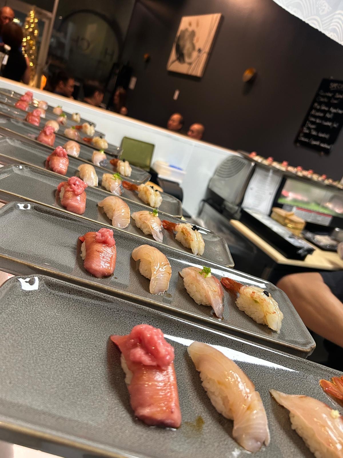 Multiple trays of sushi with various types of fish and toppings in a restaurant setting.