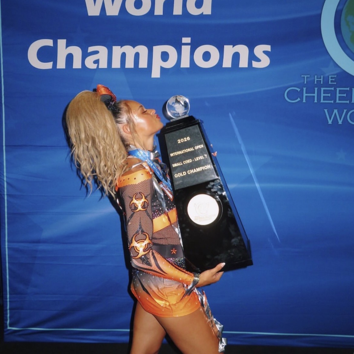 A gymnast holding a trophy and a smartphone, celebrating at a competition with a blue backdrop.