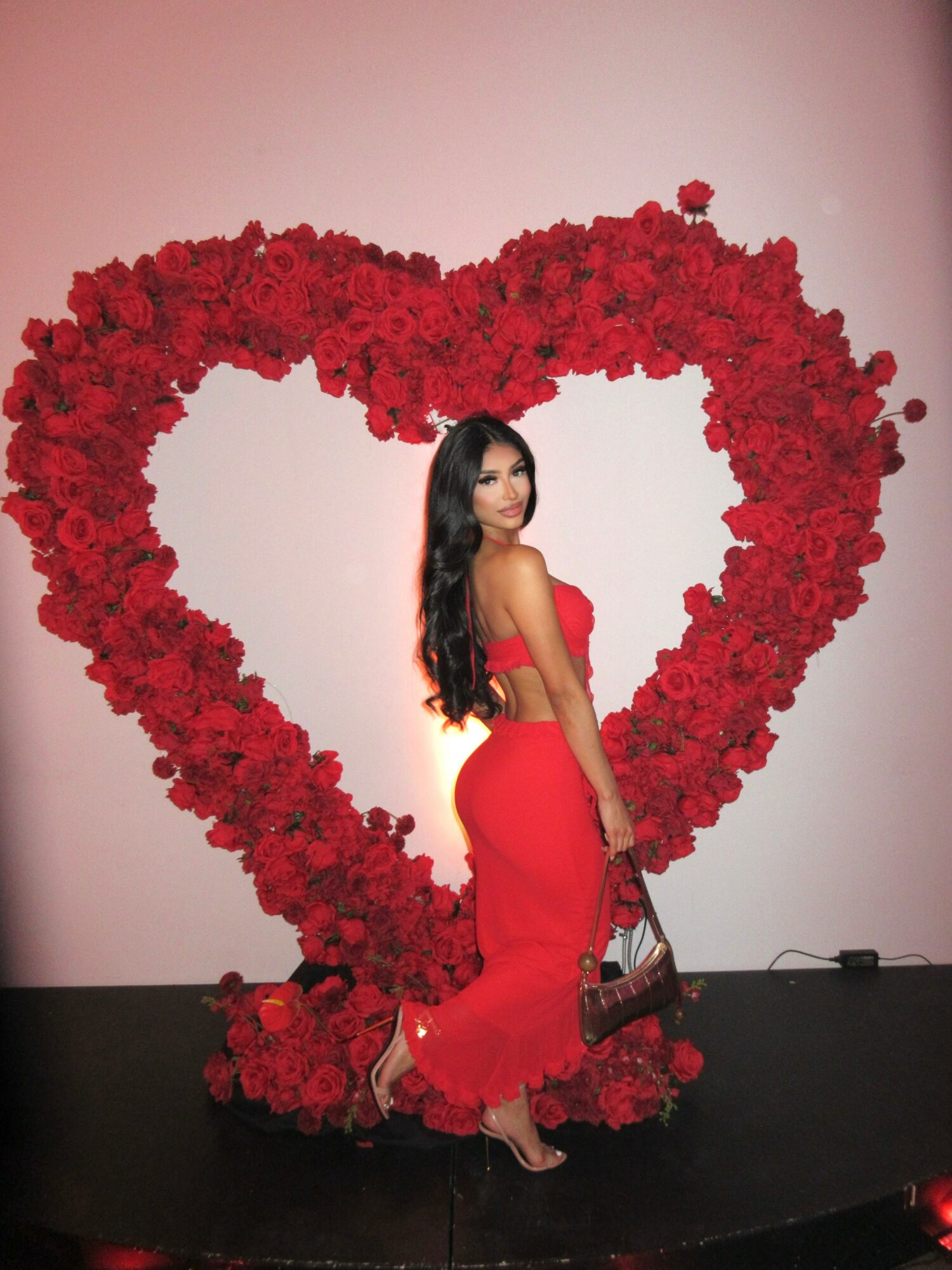 Woman in red dress standing in front of a large heart-shaped flower arrangement.