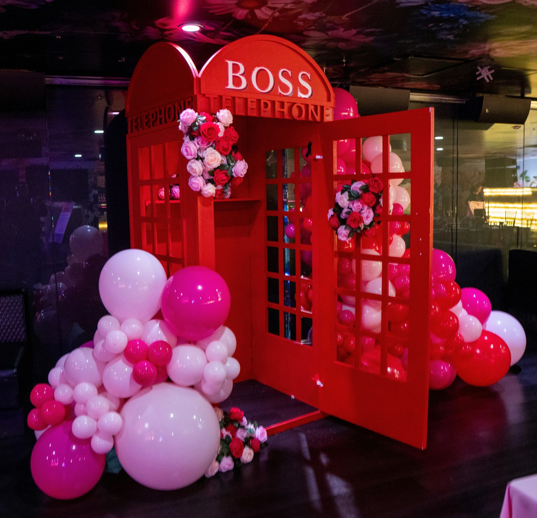 Red phone booth with flowers and balloons, with a sign reading 'BOSS' at the top.