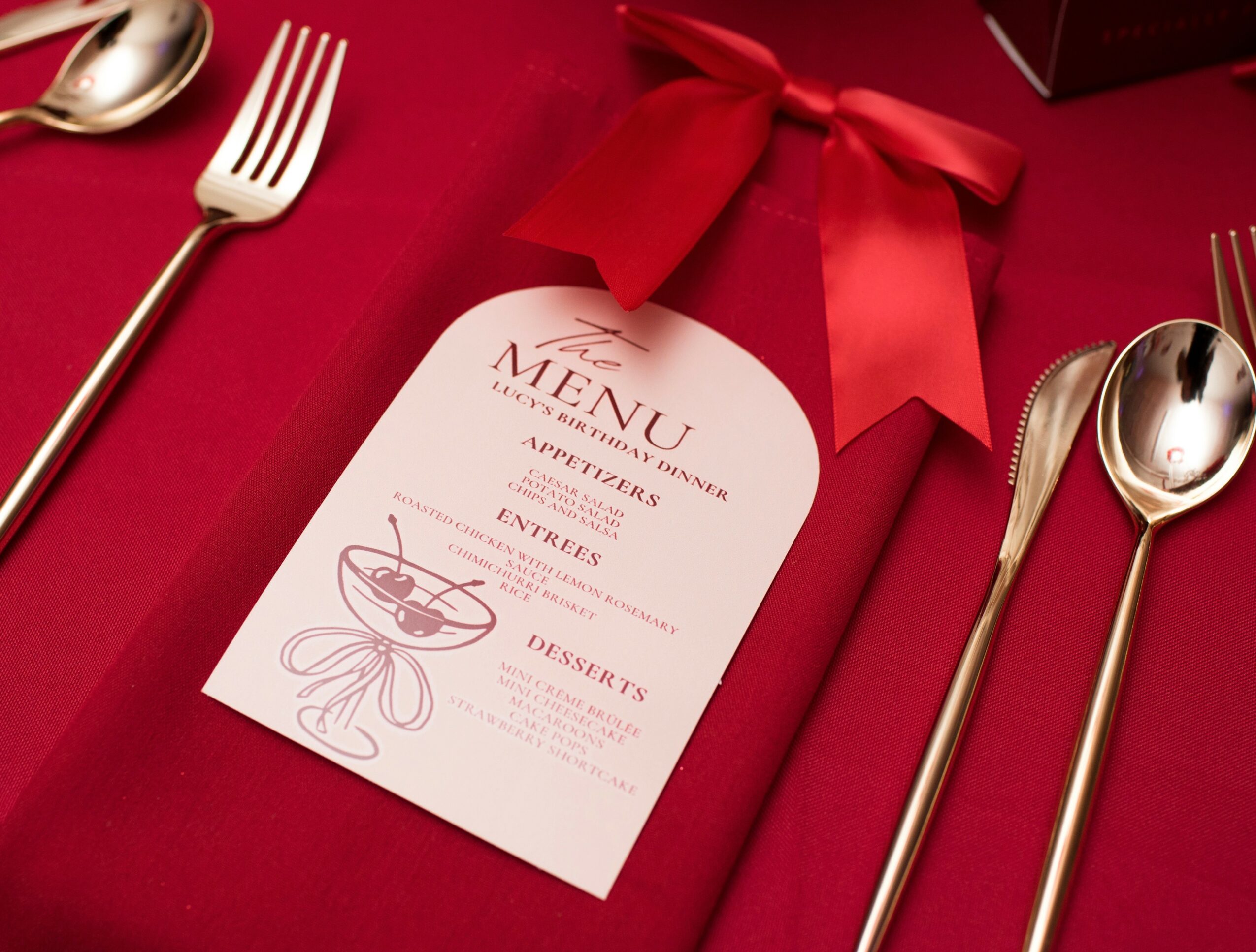 Menu card on red tablecloth with gold cutlery and a red ribbon bow.