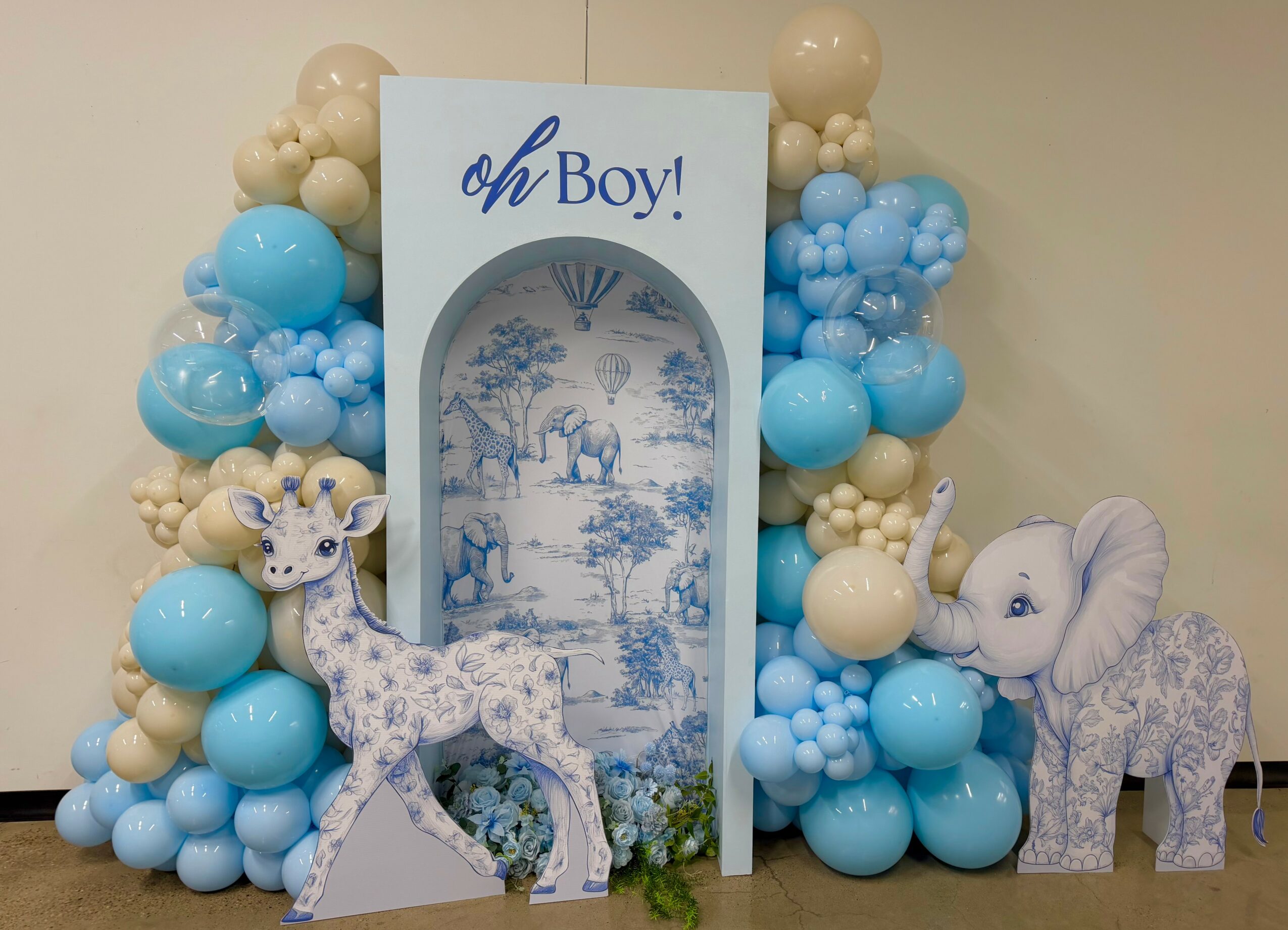 Decorative display with blue and beige balloons, a sign reading 'oh Boy!', and two plush giraffe toys.