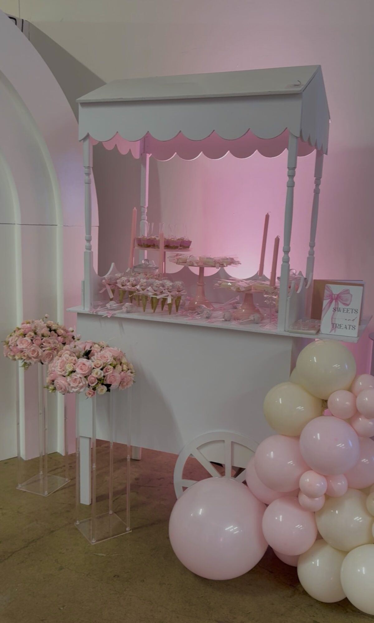Pink and white balloon arrangement with a dessert cart and floral display in a decorated setting.