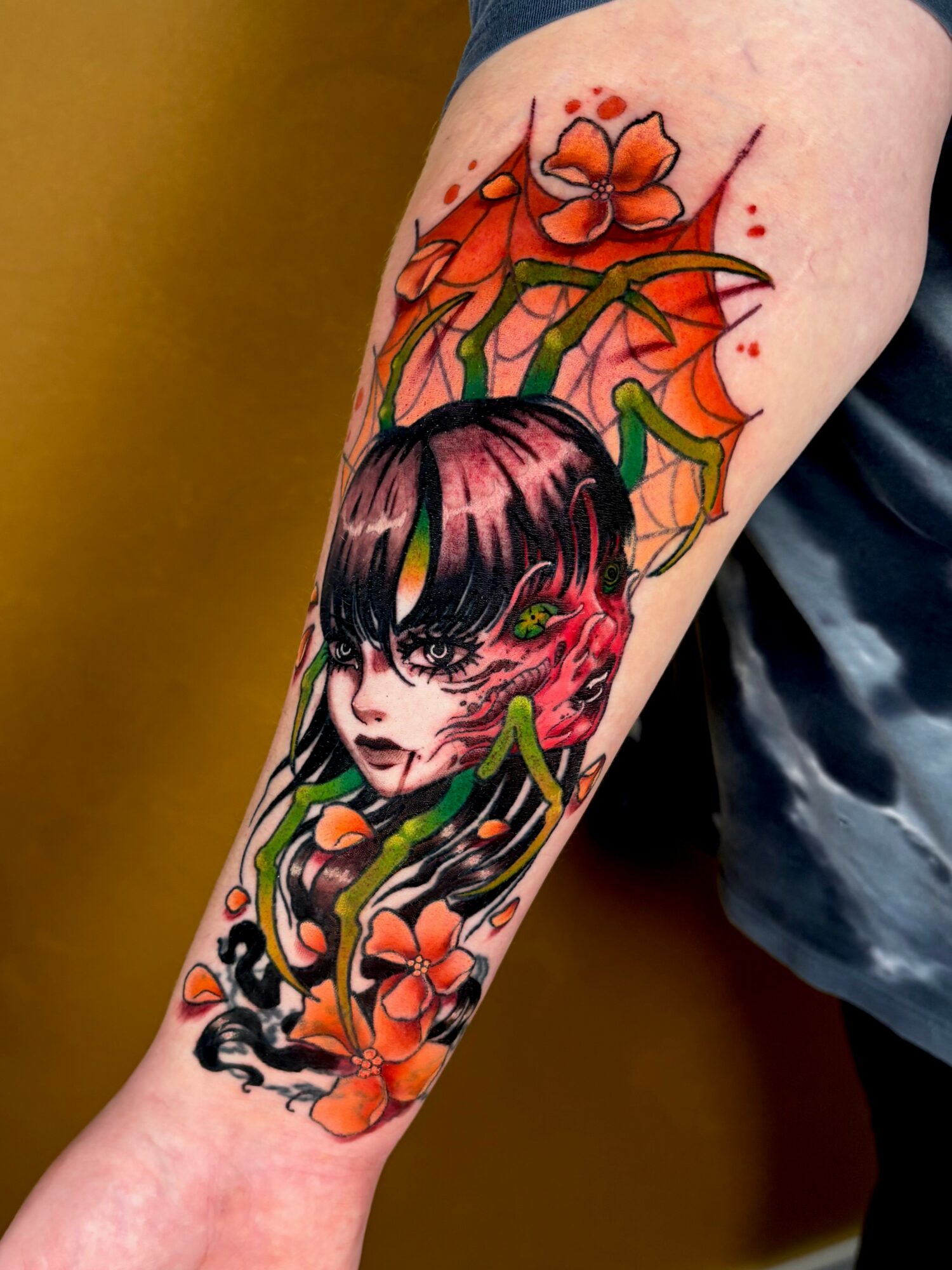 Tattoo of a girl with dark hair, surrounded by orange flowers and green leaves, on person's arm.