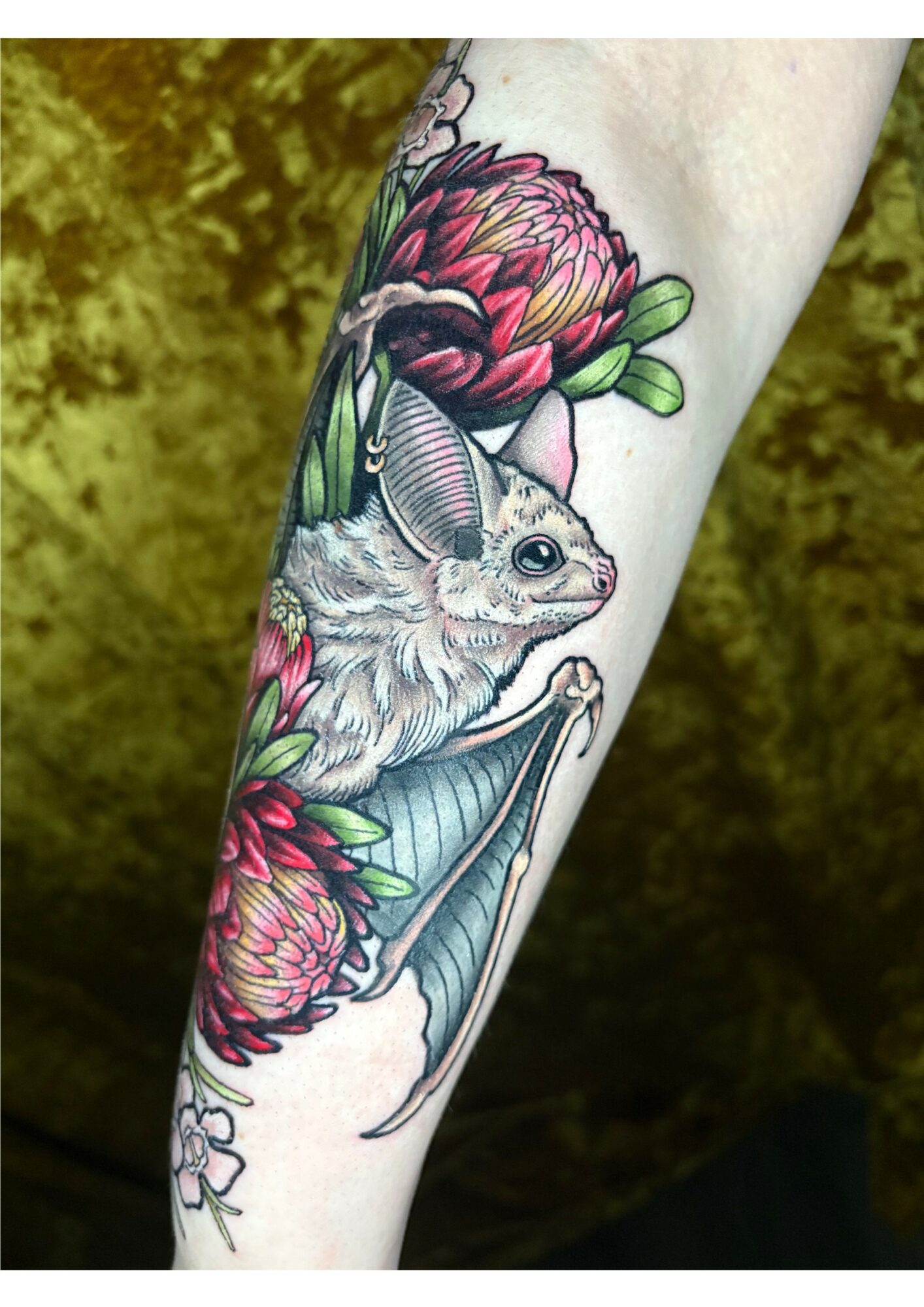 Detailed rabbit tattoo surrounded by pink flowers and green leaves on person's arm.