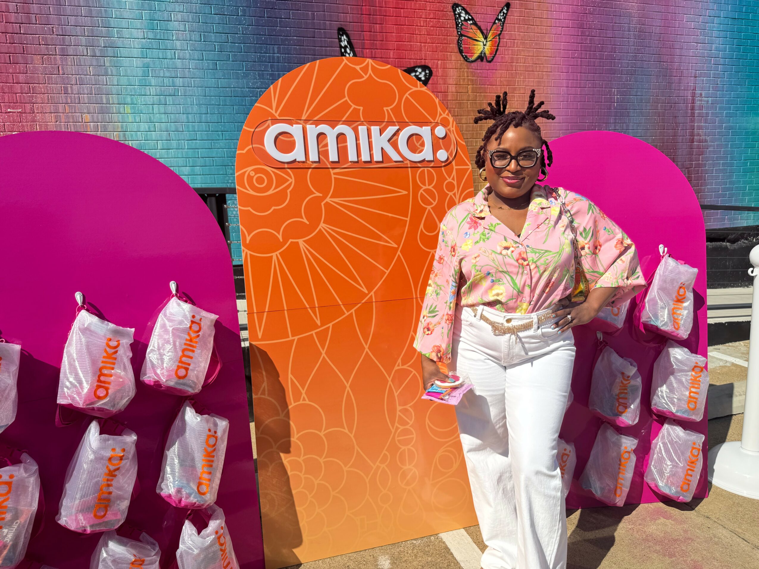 Woman standing next to orange and pink display panels with bags, smiling, colorful background.