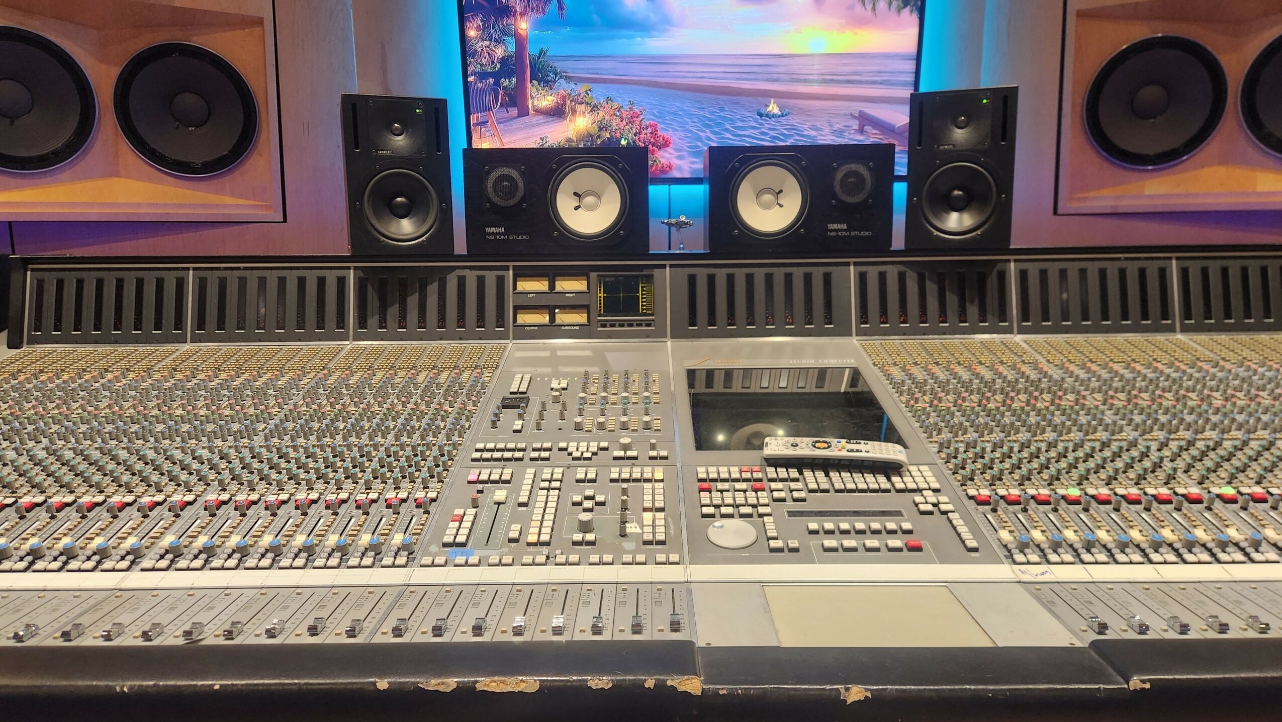 Recording studio mixing console with numerous controls and speakers, and a computer monitor in the background.