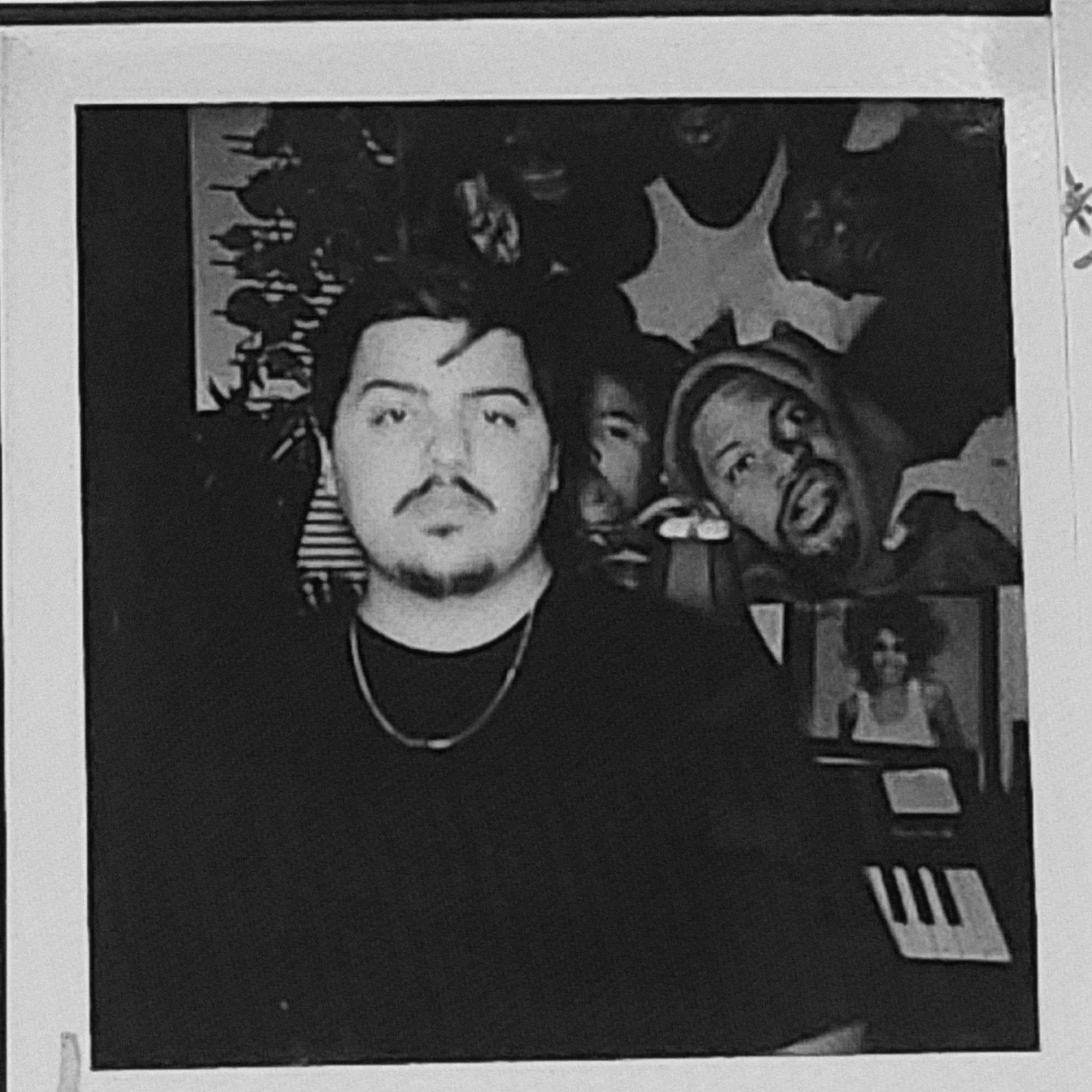 Group of people, some making faces, in a room with a star and plant decoration, and a keyboard in the background.