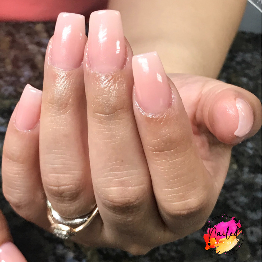 Hand with well-manicured nails painted in light pink, wearing a ring on the ring finger, against a dark background.