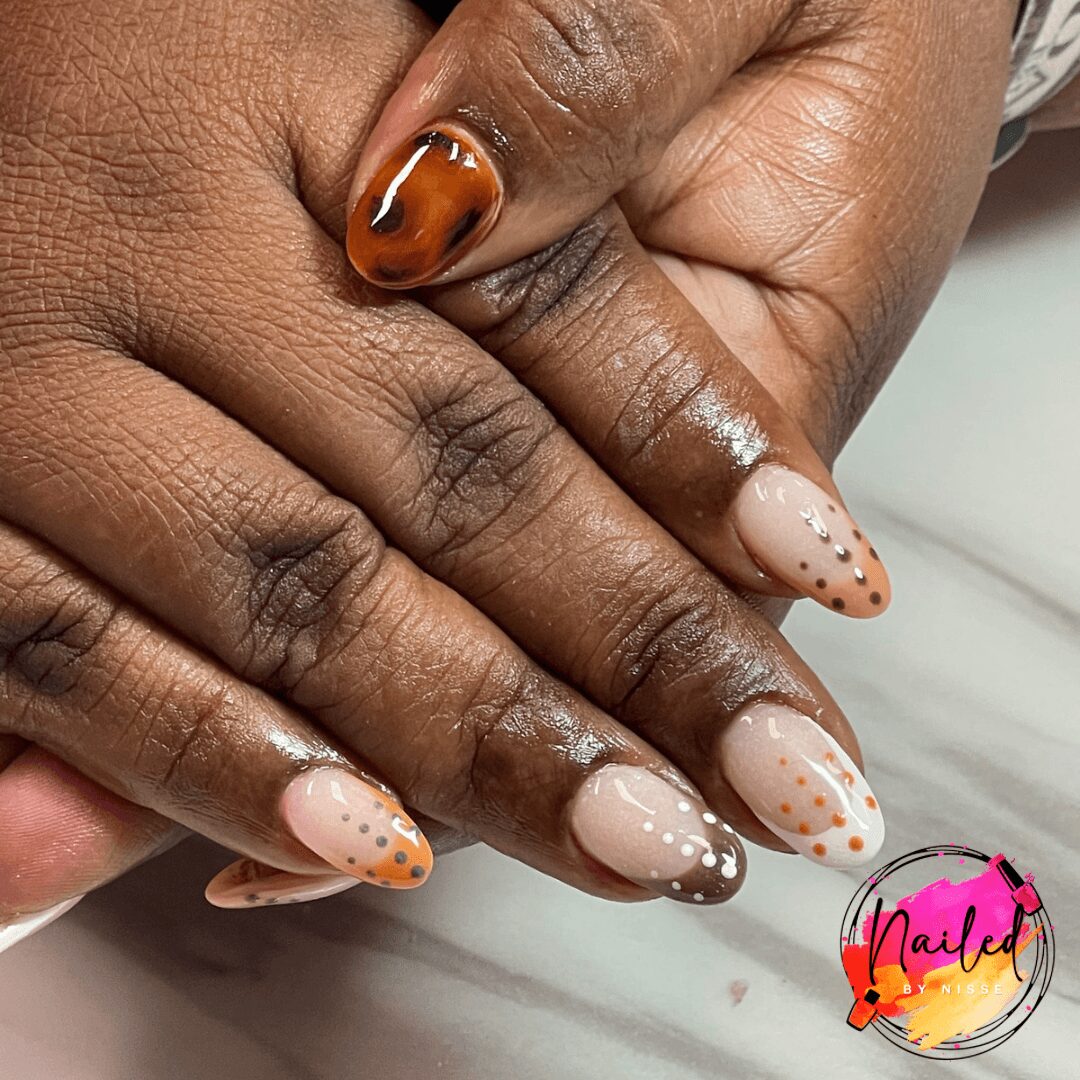 Close-up of two hands with manicured nails, one with orange and black design, the other with light pink and dotted pattern.