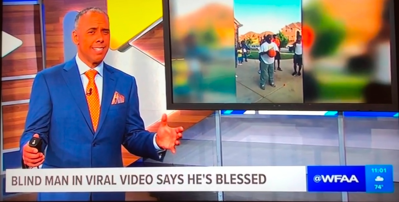 TV news anchor in blue suit and orange tie speaking with a large screen behind him showing outdoor scene.