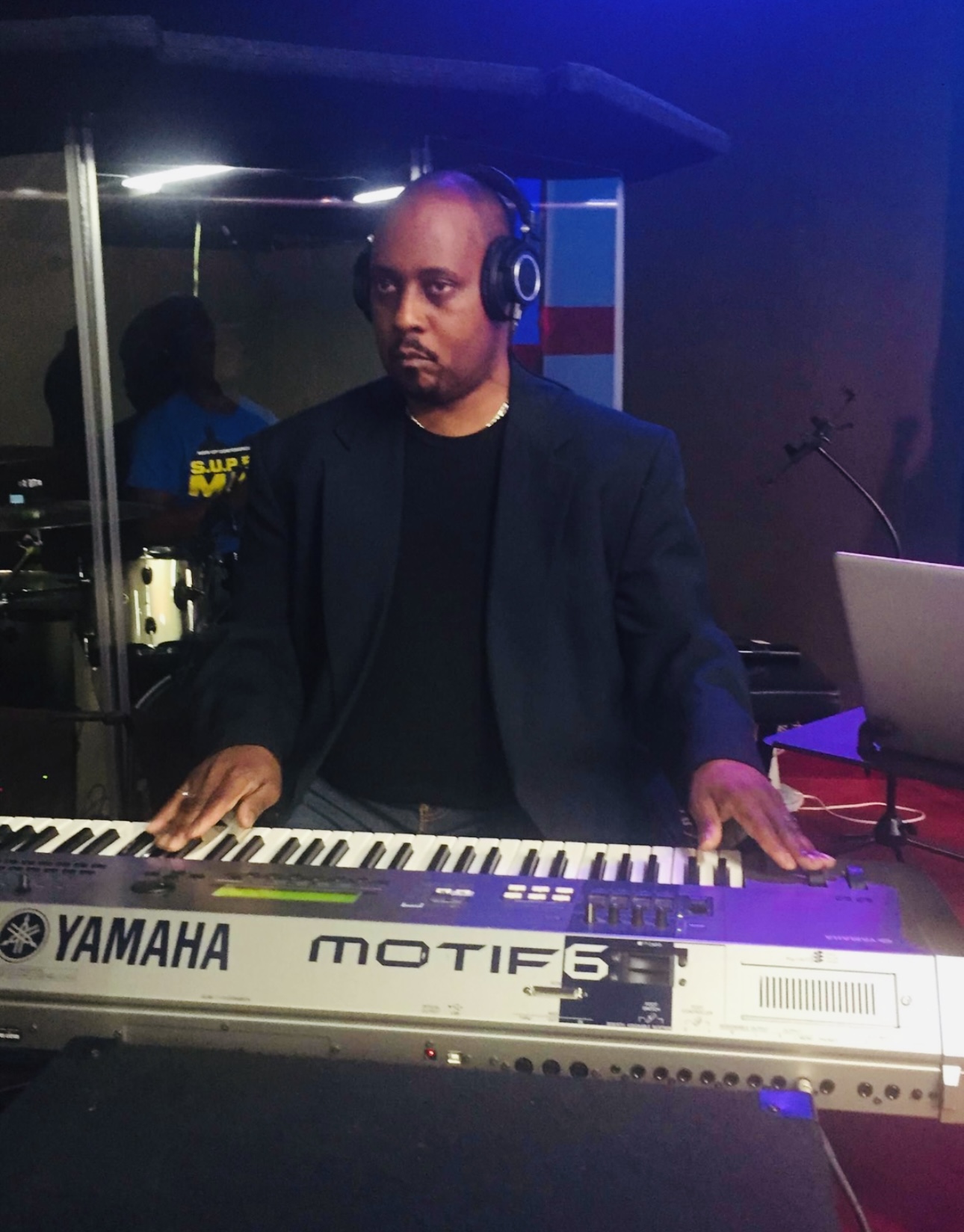 Man wearing headphones playing a Yamaha Motif 6 keyboard in a dimly lit room.