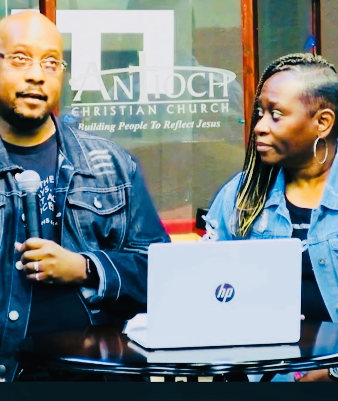 Man and woman speaking at a church event with a laptop on a table.