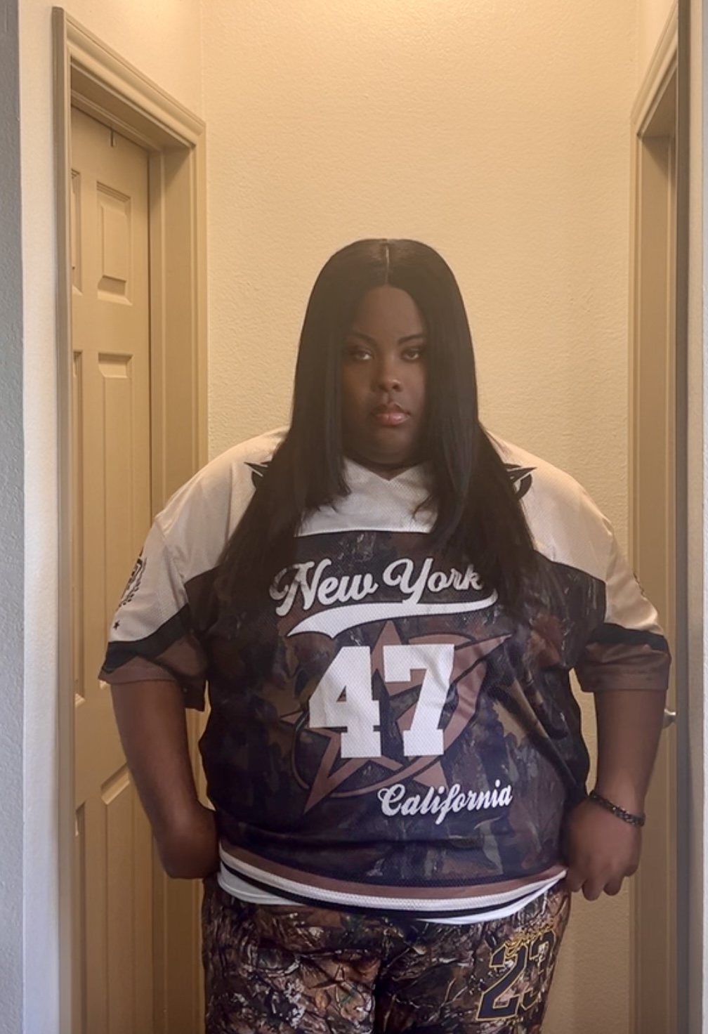 Person standing in hallway wearing a black and white sports jersey with 'New York 47 California' text.