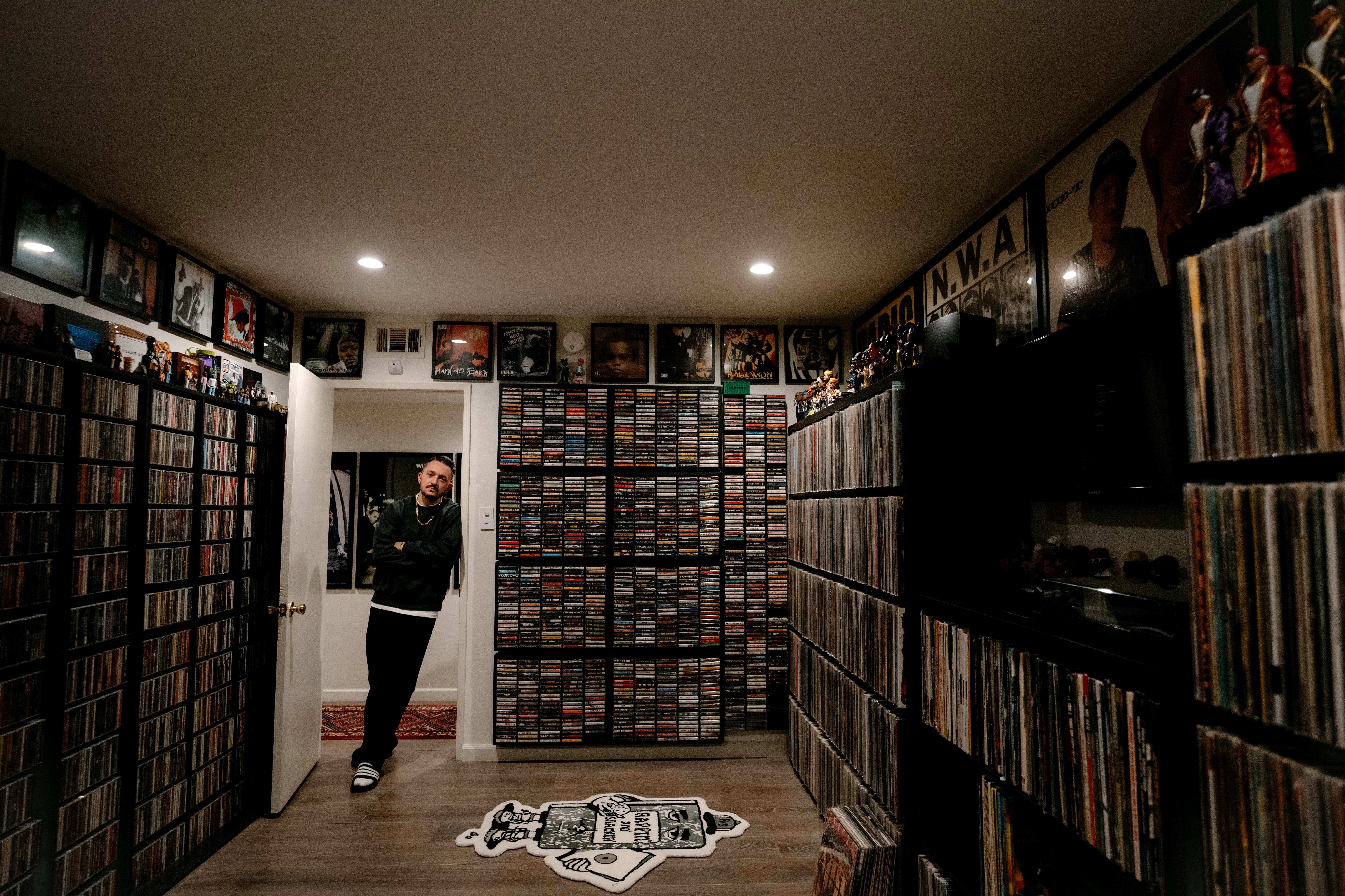 Person standing in a room with shelves filled with DVDs or CDs, doorway visible, carpet with logo on the floor.