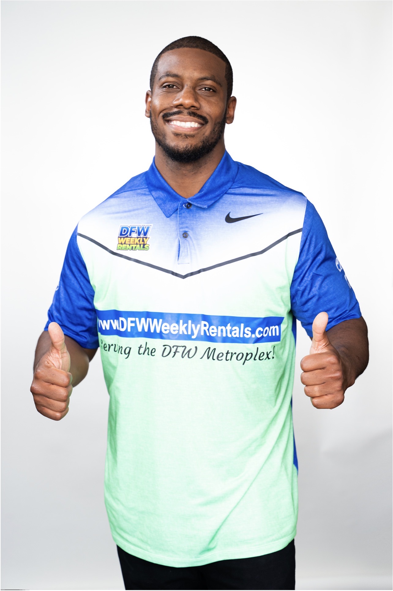 Smiling man in sports jersey giving two thumbs up against a plain background.