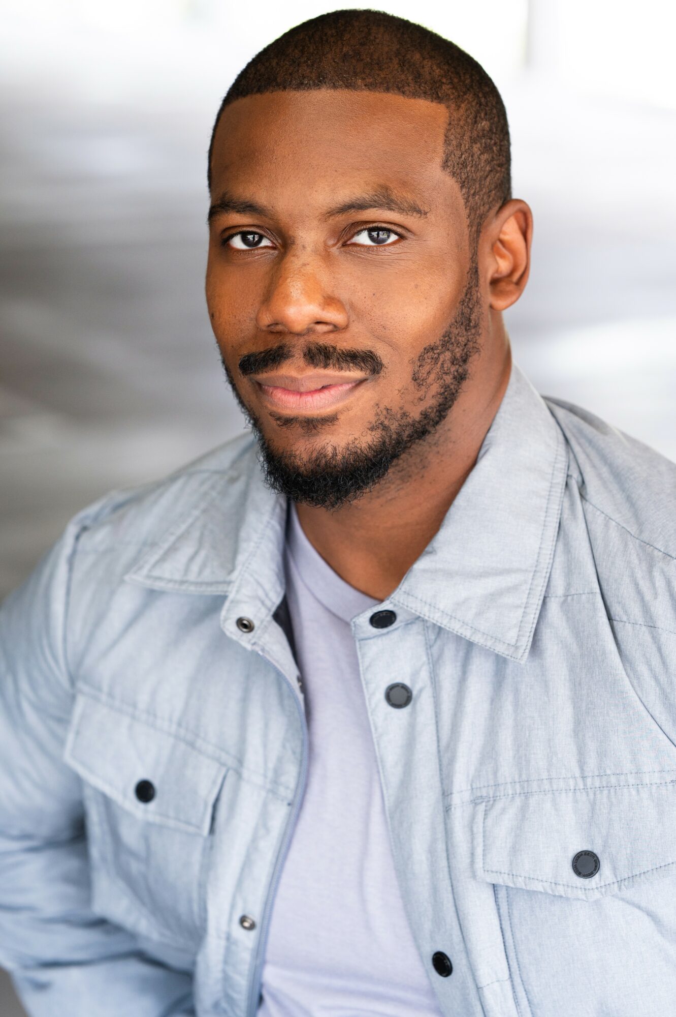 Portrait of a man with short hair, beard, wearing a light gray shirt, smiling softly, neutral background.