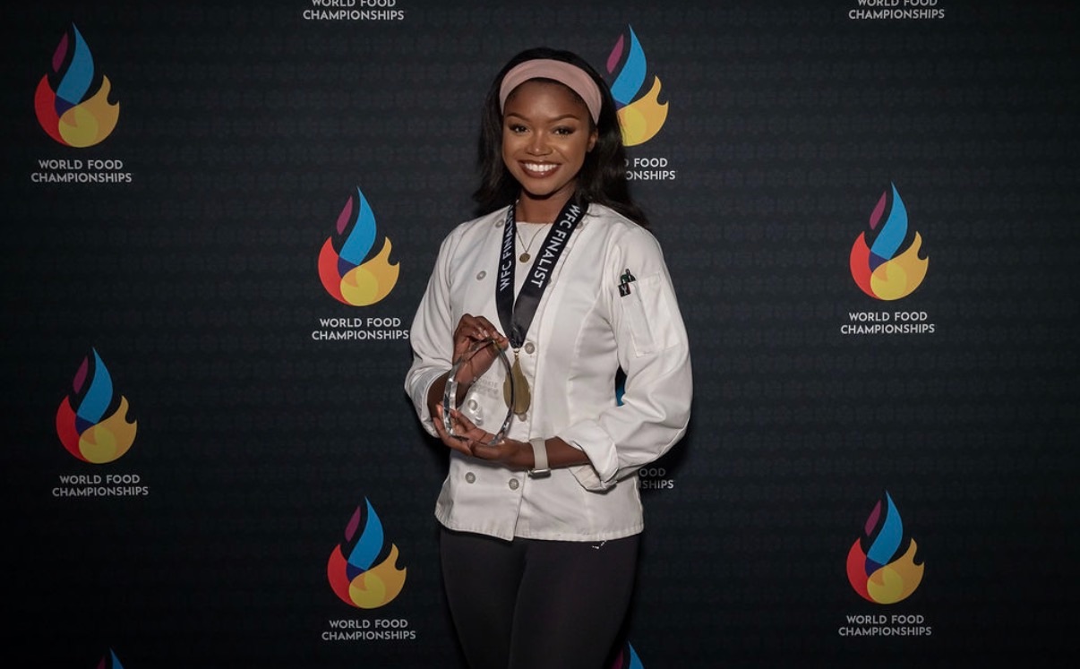 Smiling woman holding a trophy in front of a dark background with colorful flame logos.