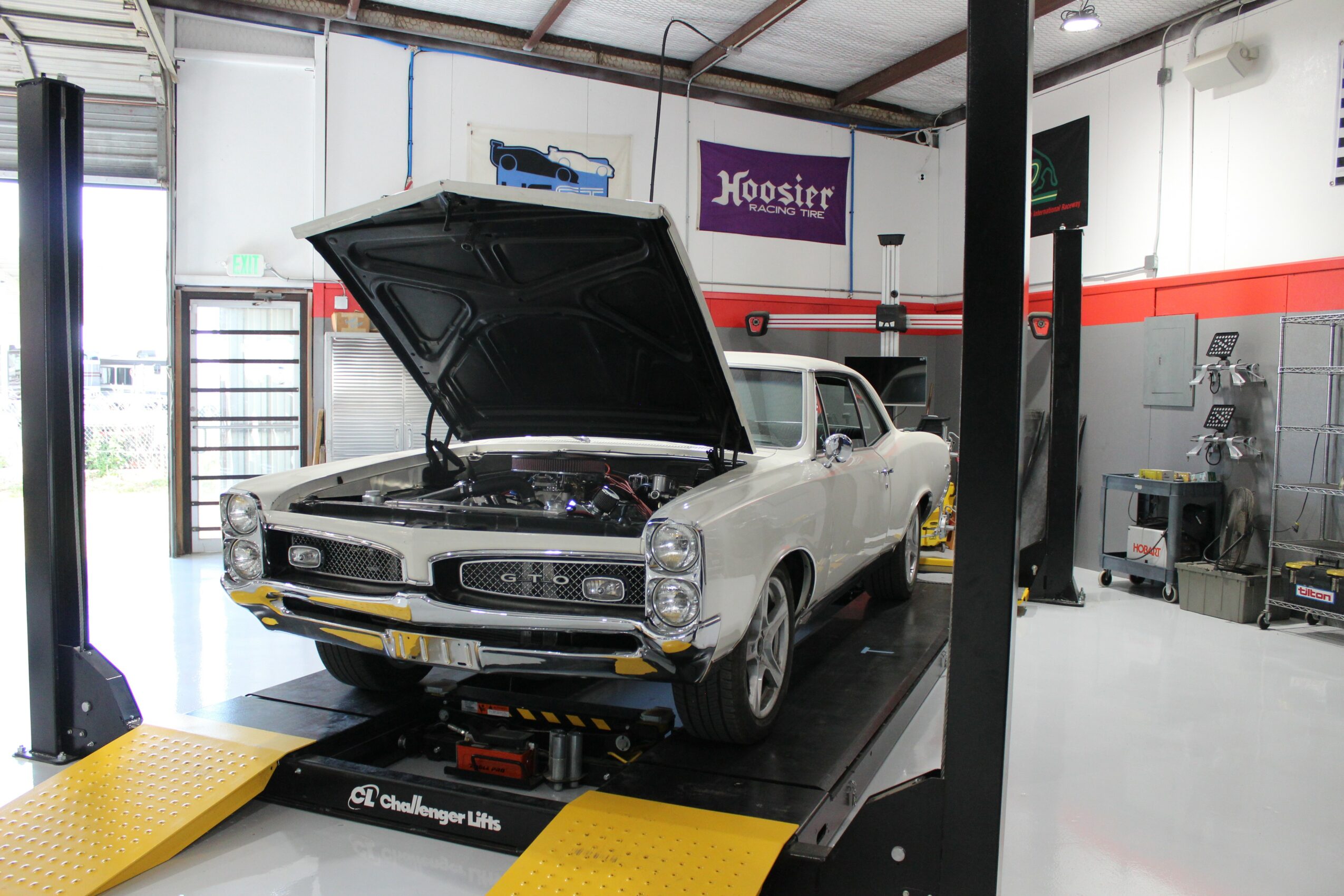 Classic white car with open hood on a lift inside a garage or workshop.