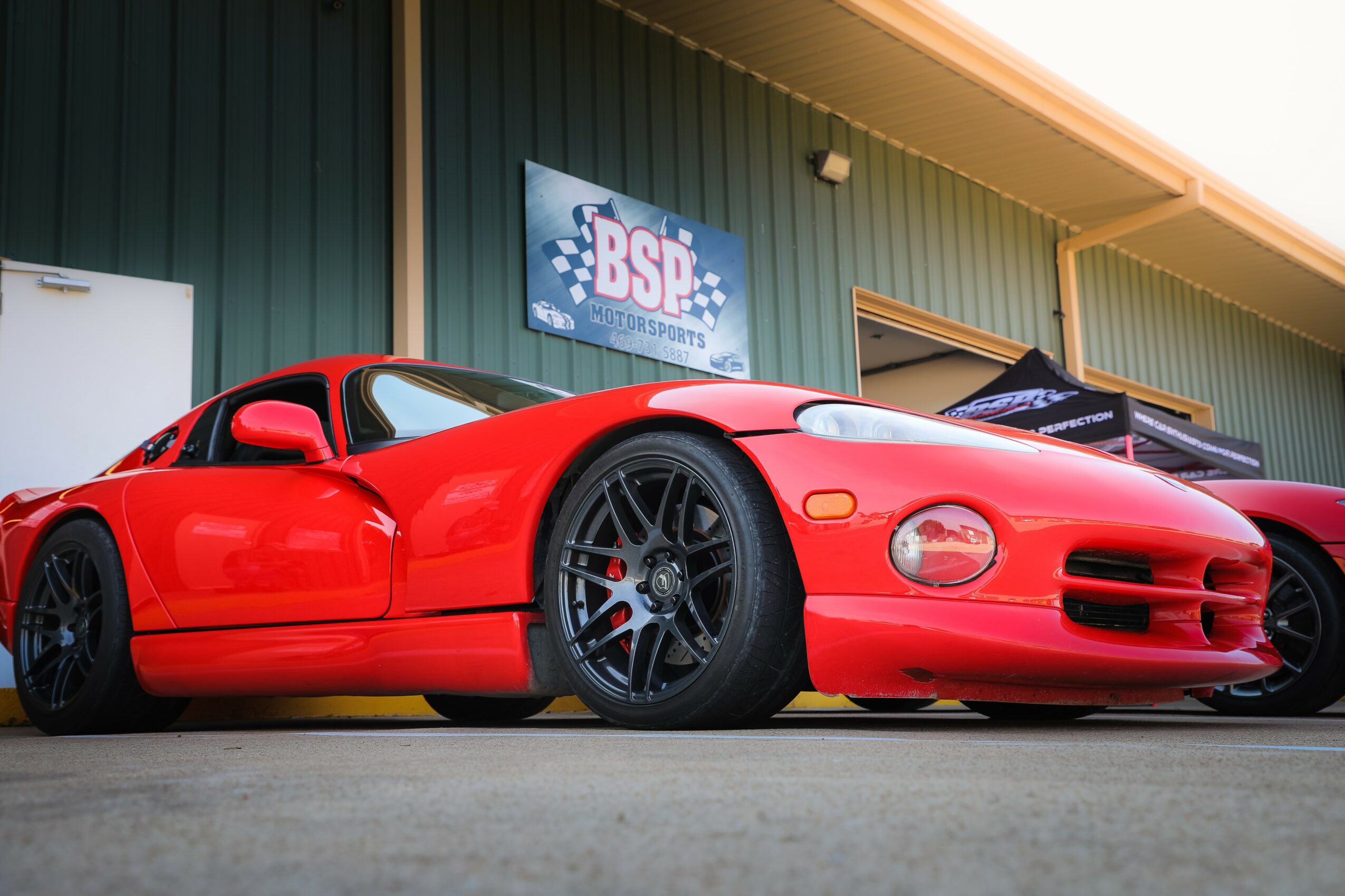 Red sports car parked outside a building with a sign reading 'BSF'.