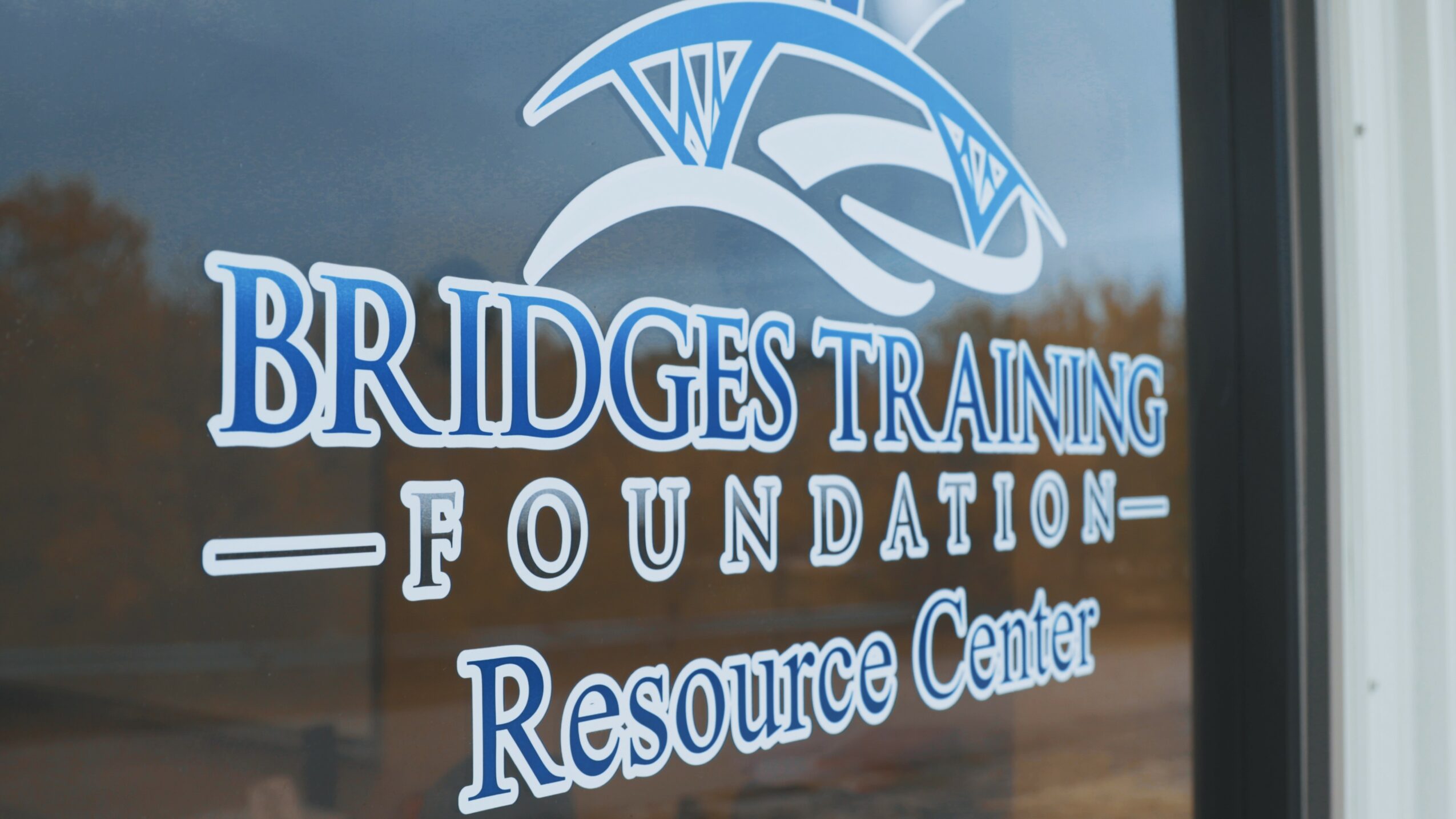 Sign for Bridges Training Foundation Resource Center with logo and text on glass window.