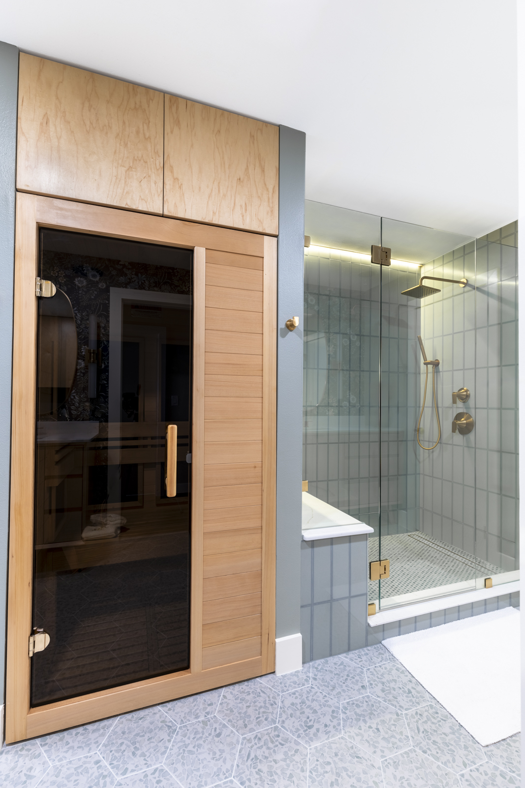 Sauna door with glass panel next to a glass shower enclosure with a showerhead and fixtures.