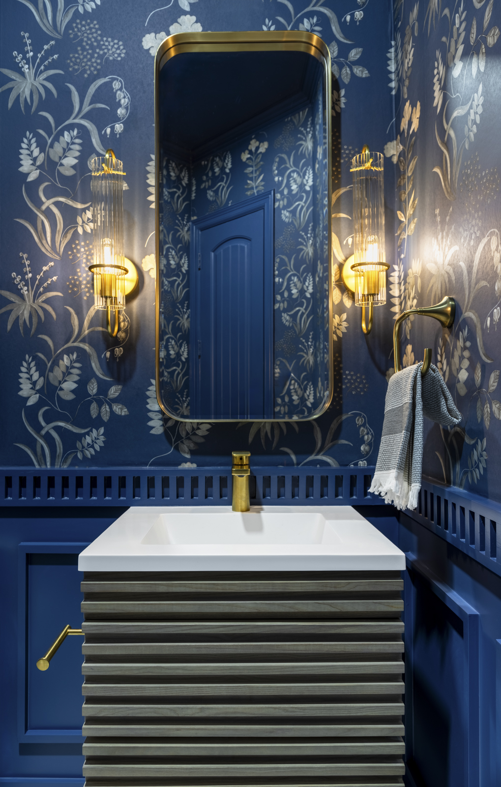 Bathroom sink with a mirror, blue patterned wallpaper, and wall-mounted lights on each side.