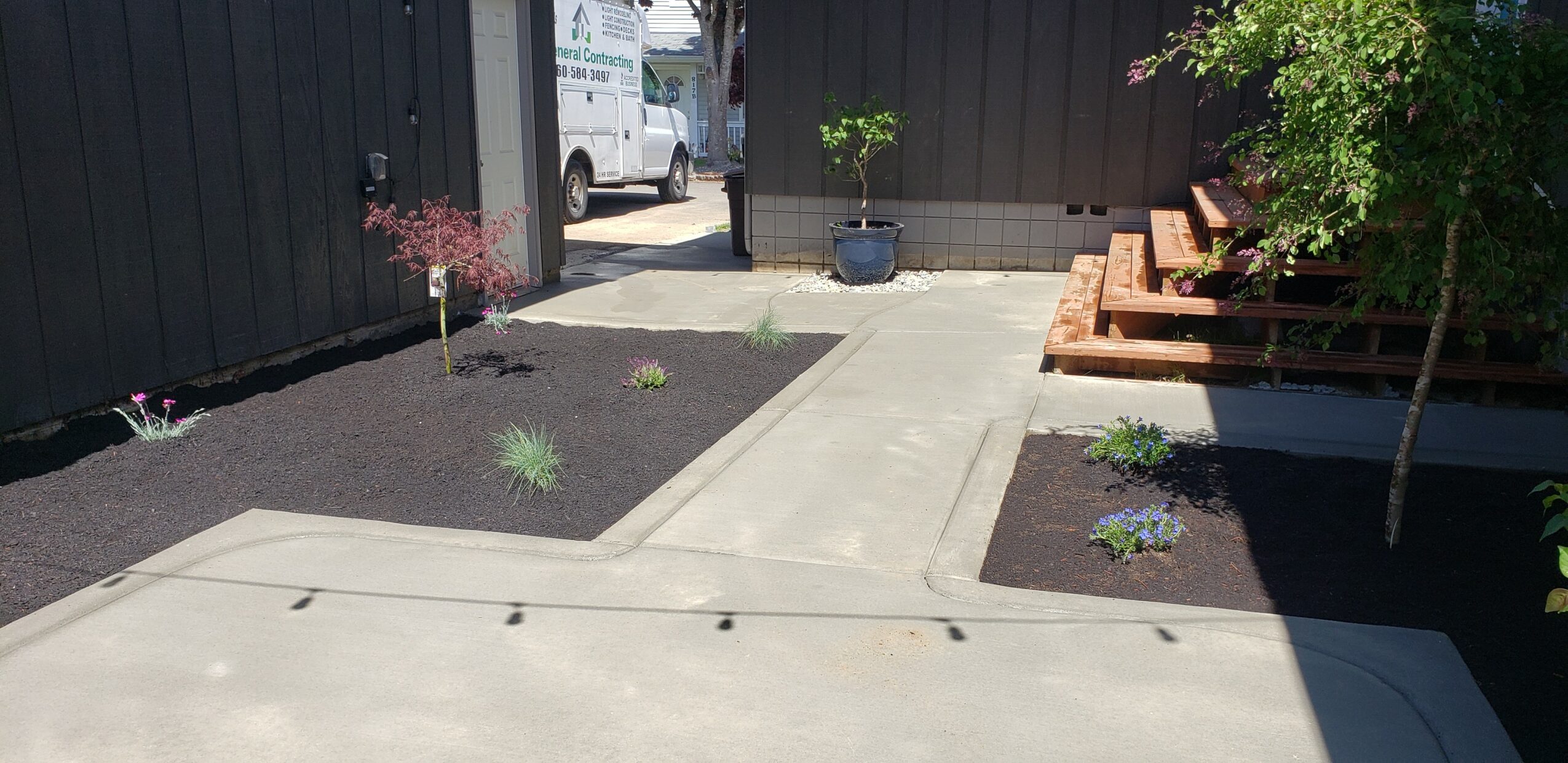 Concrete sidewalk with garden beds on both sides, potted plant, and wooden bench on right side.