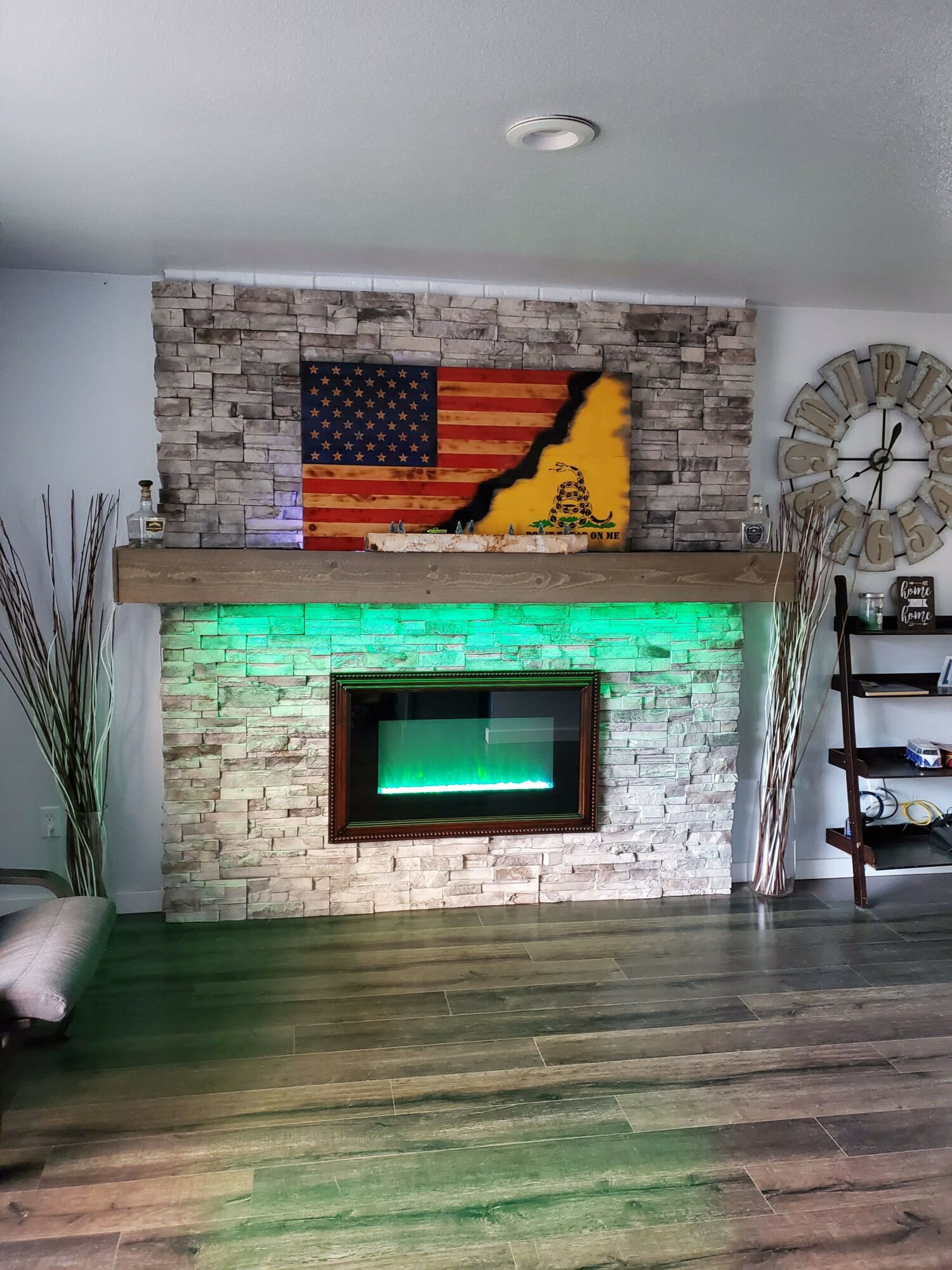 Living room fireplace with a brick surround, American flag artwork above, and green lighting below the mantel.