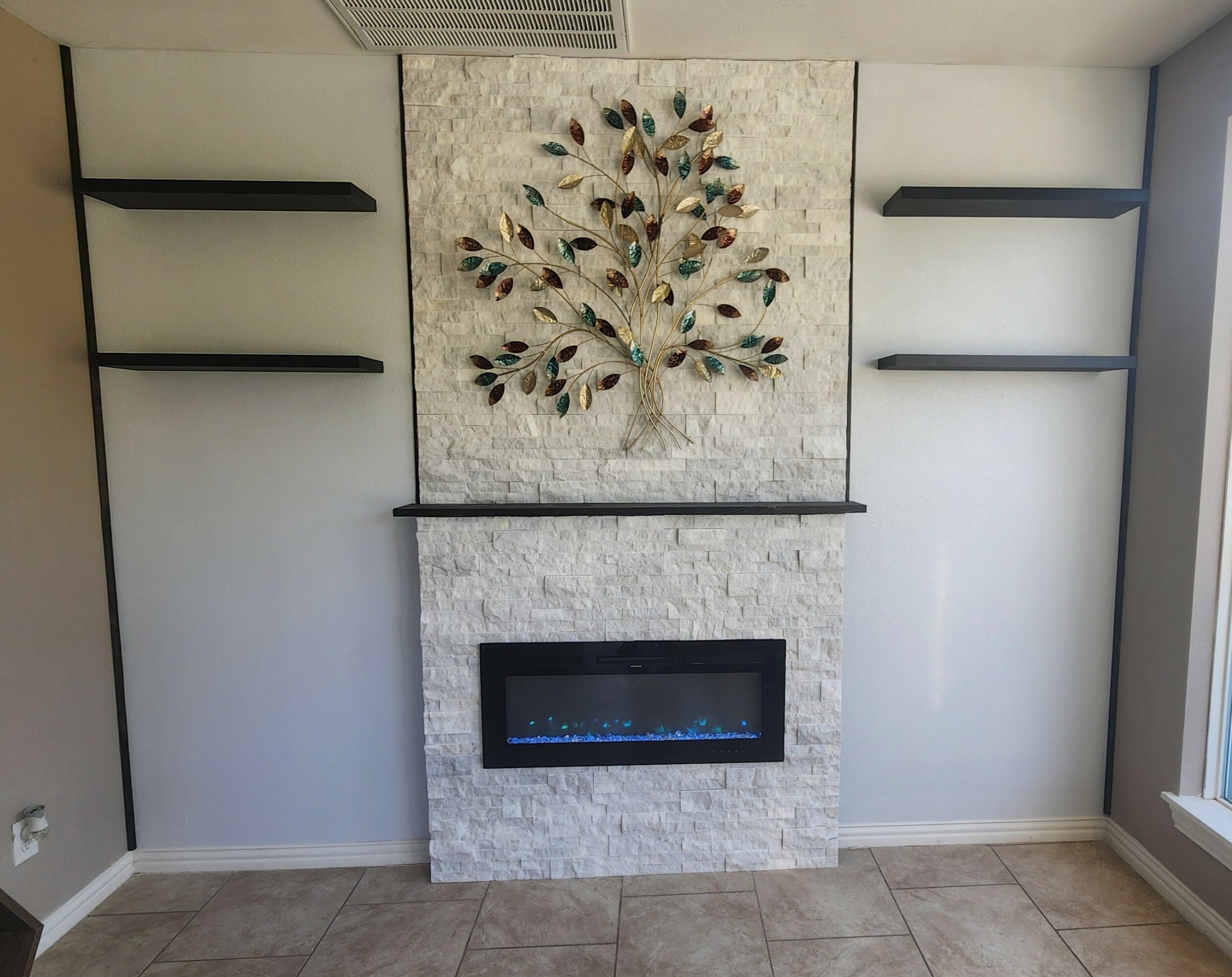 Interior wall with a fireplace, decorative tree artwork, and black shelves on white walls.